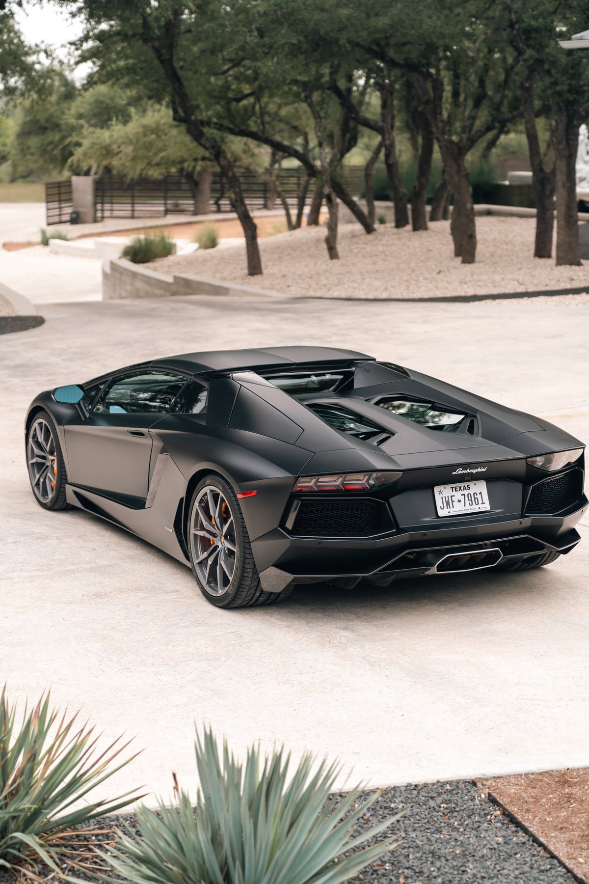 Matte black Lamborghini Aventador LP700-4 with silver multi-spoke rims and orange brake calipers.
