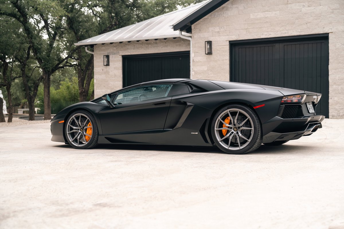 Matte black 2014 Lamborghini Aventador LP700-4 with gray rims and orange brake calipers.