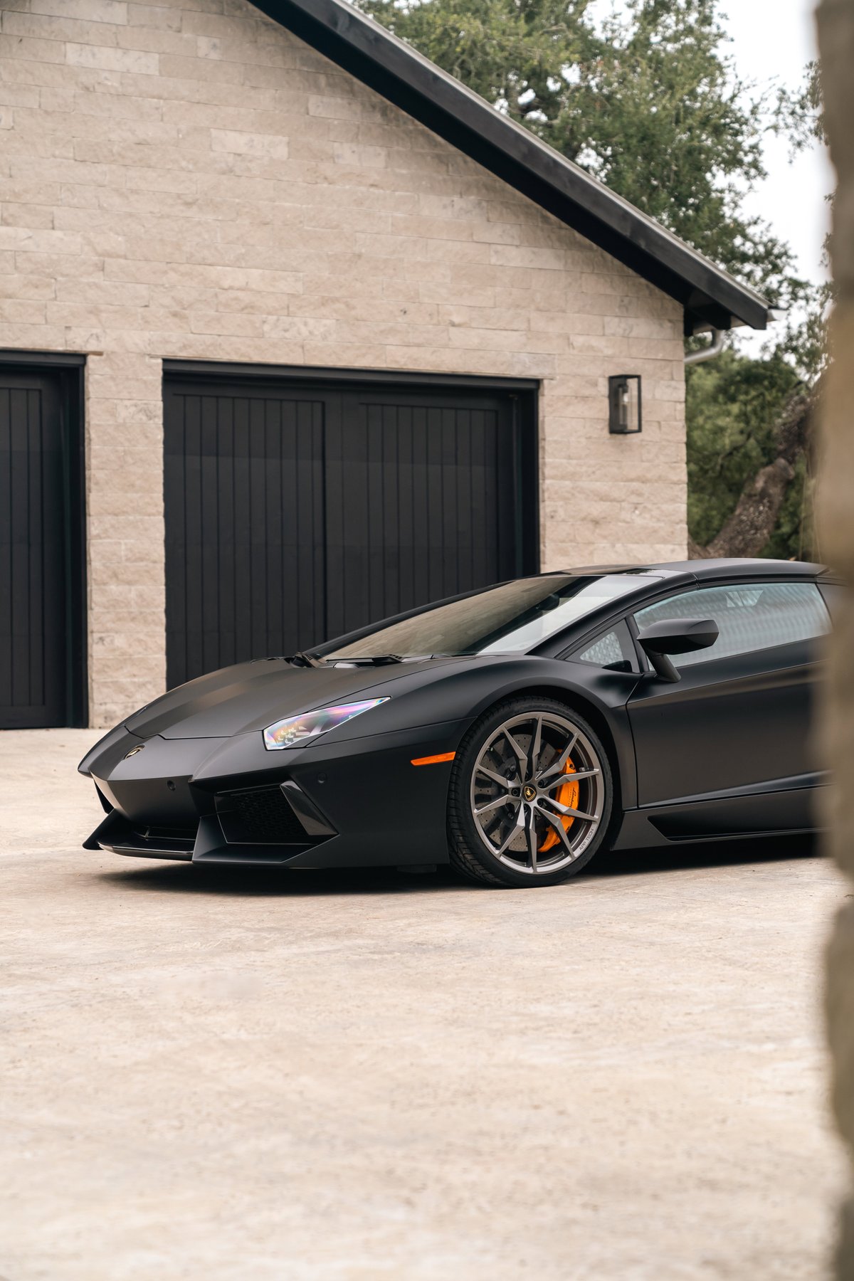 Matte black Lamborghini Aventador LP700-4 with orange brake calipers and grey multi-spoke rims.