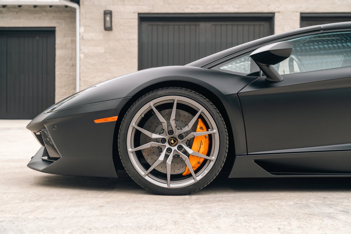 Matte black Lamborghini Aventador LP700-4 wheel with orange brake calipers and silver rims.