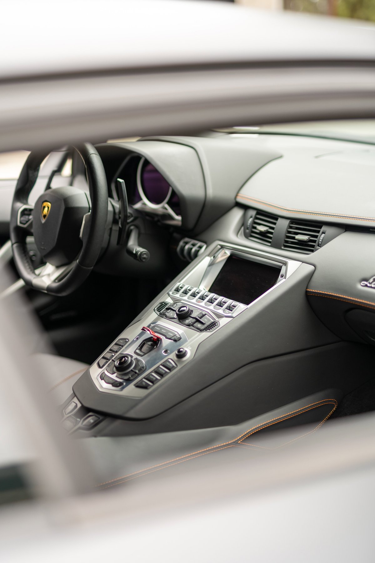 Lamborghini Aventador LP700-4 interior featuring carbon fiber trim, leather seats with orange stitching, and a central console.