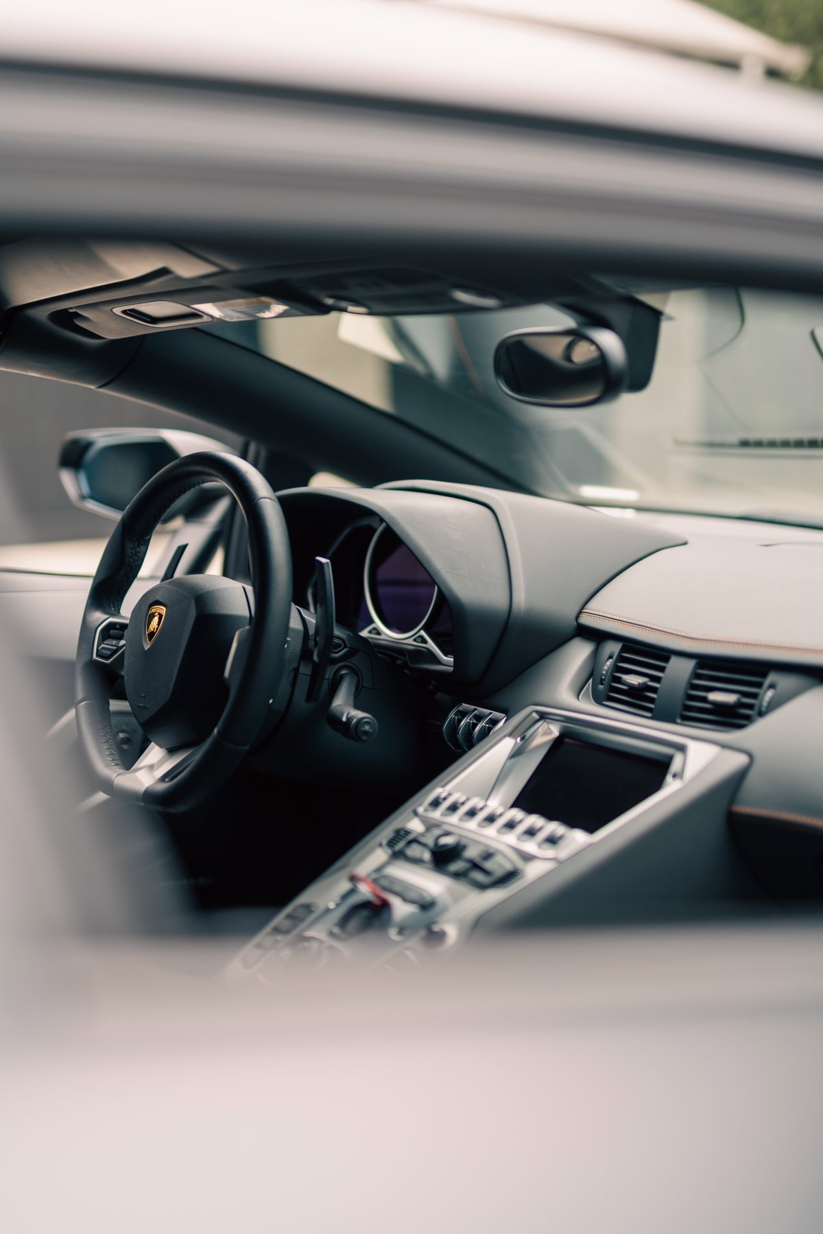 Interior view of a Lamborghini Aventador LP700-4 dashboard, featuring a leather-wrapped steering wheel and center console.