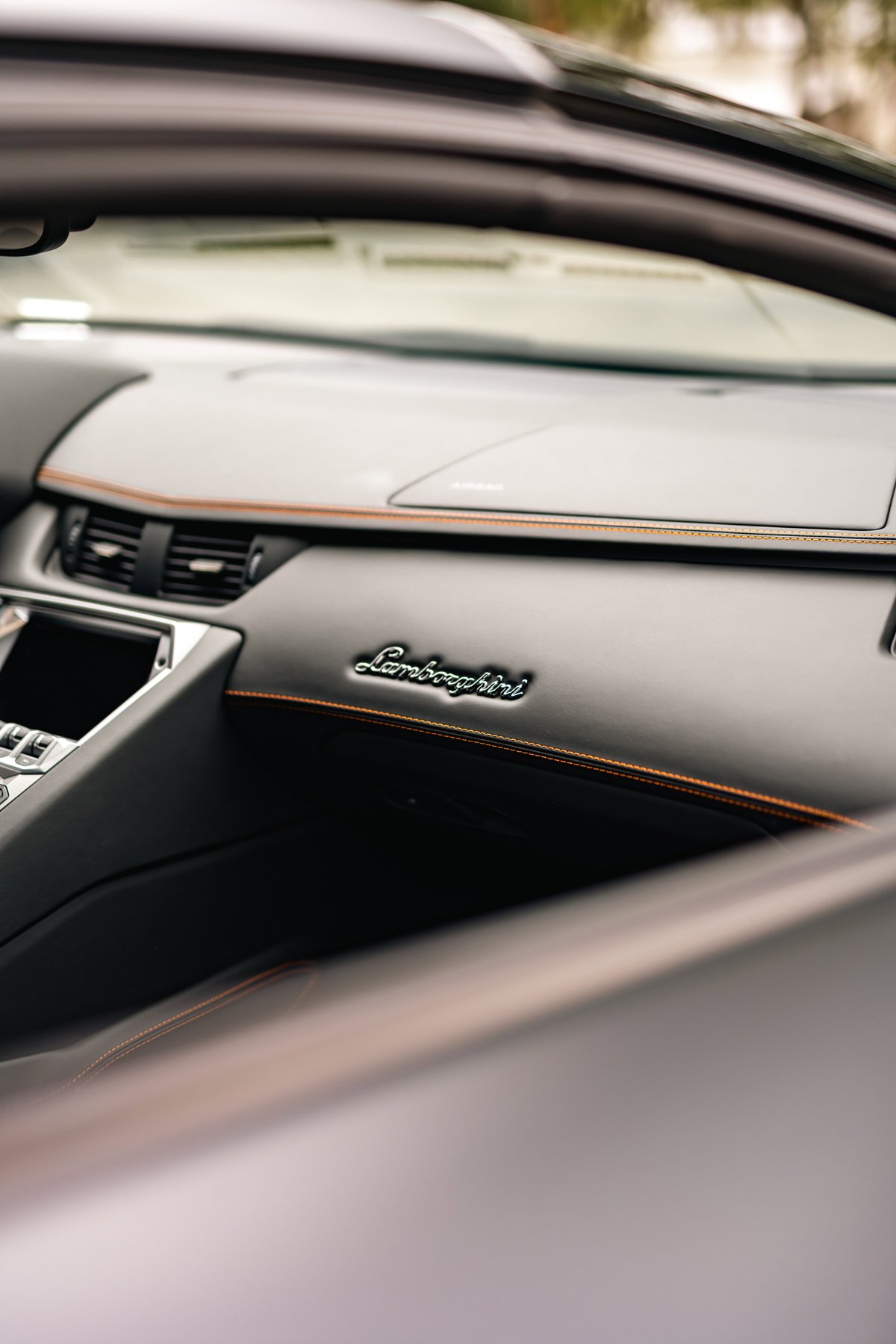 Interior of a black Lamborghini Aventador LP700-4 with orange stitching and embossed logo.