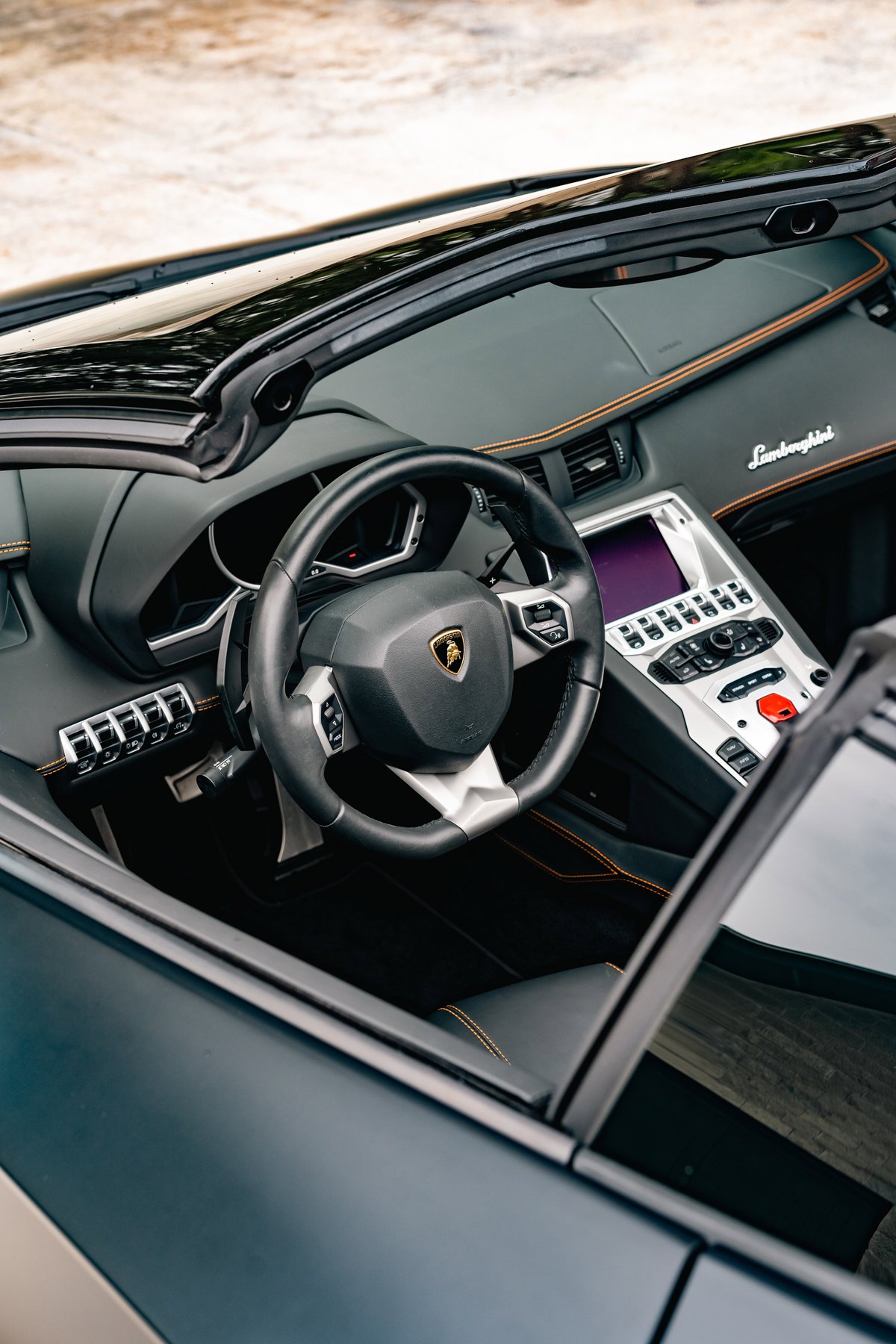 Lamborghini Aventador LP700-4 interior with orange stitching trim and infotainment screen.