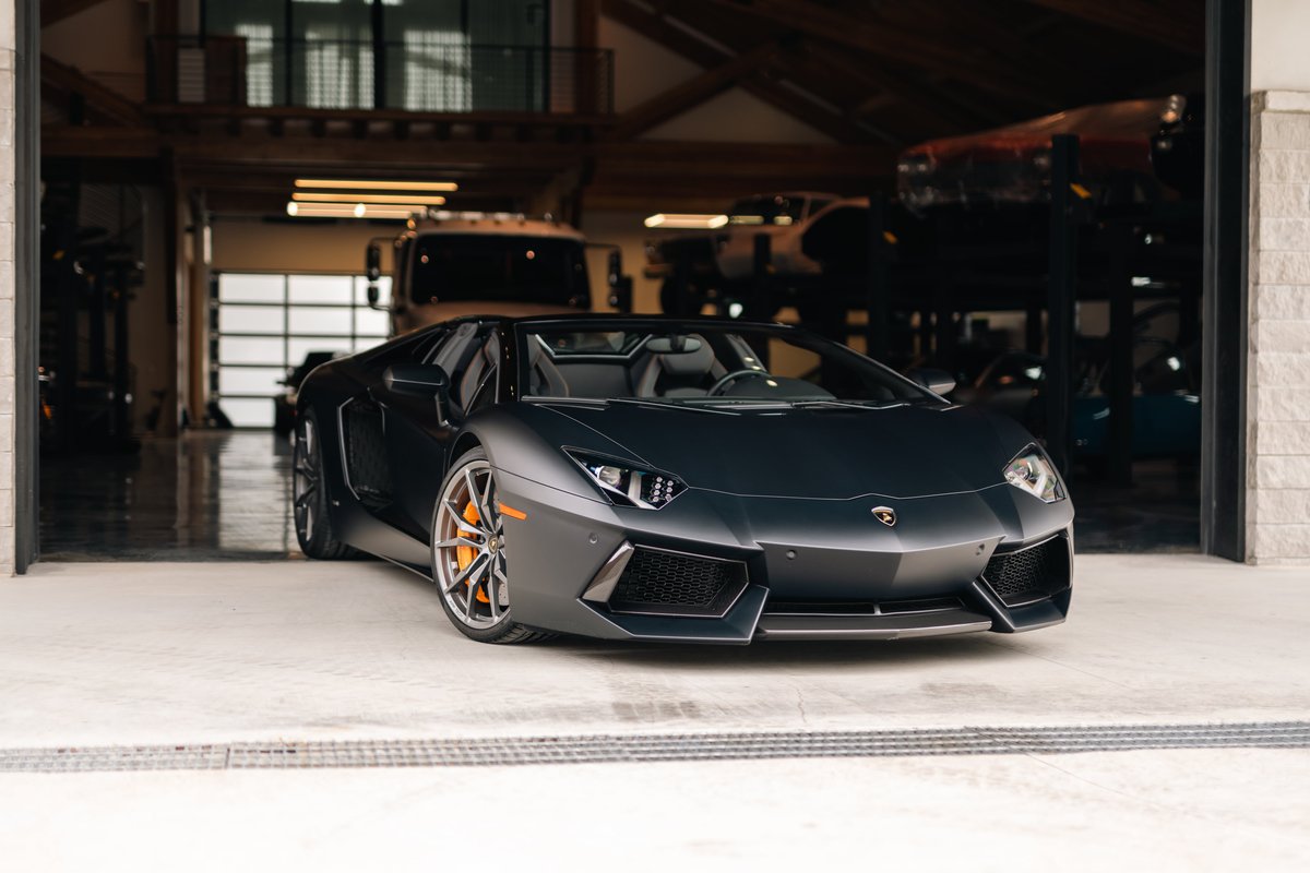 Matte black Lamborghini Aventador LP700-4 roadster with orange brake calipers and custom rims.