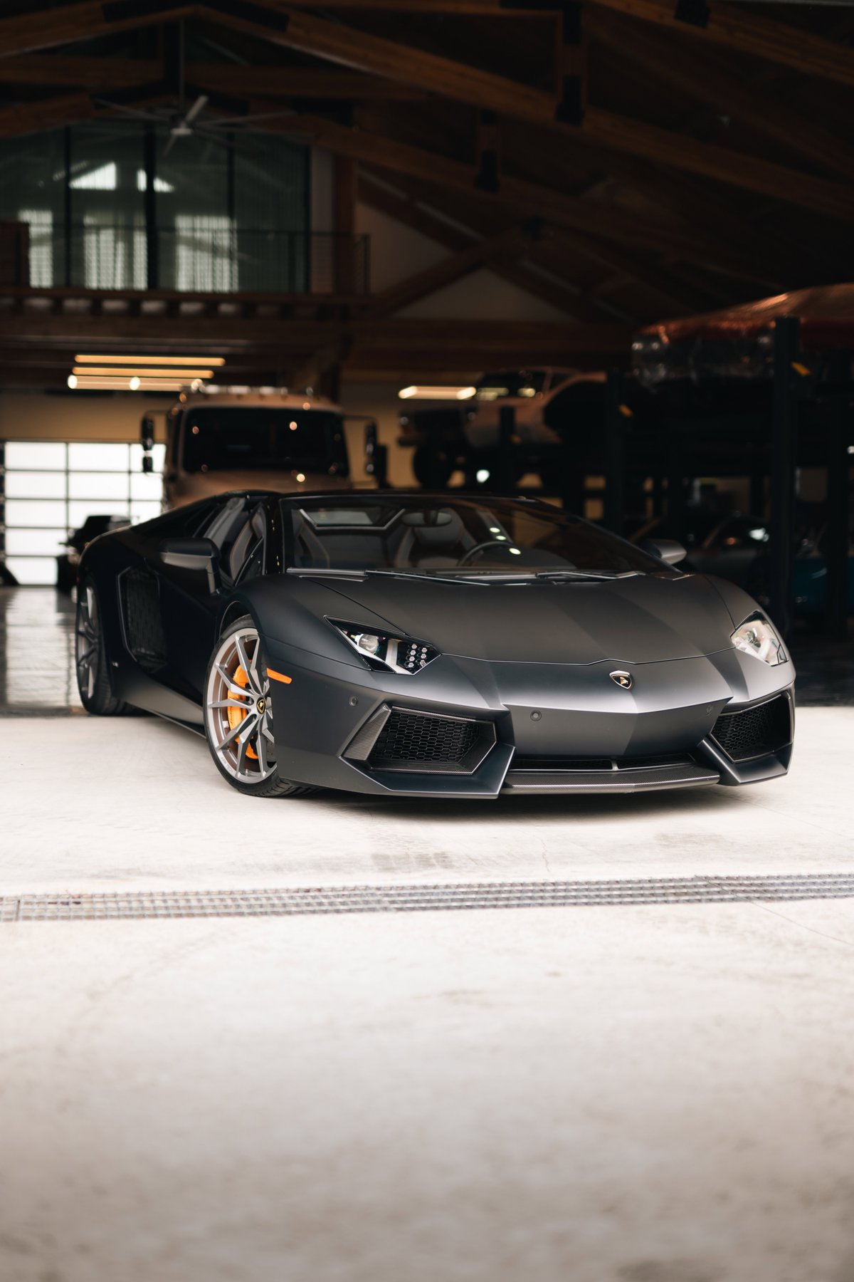 Matte black Lamborghini Aventador LP700-4 convertible with orange brake calipers and multi-spoke rims.