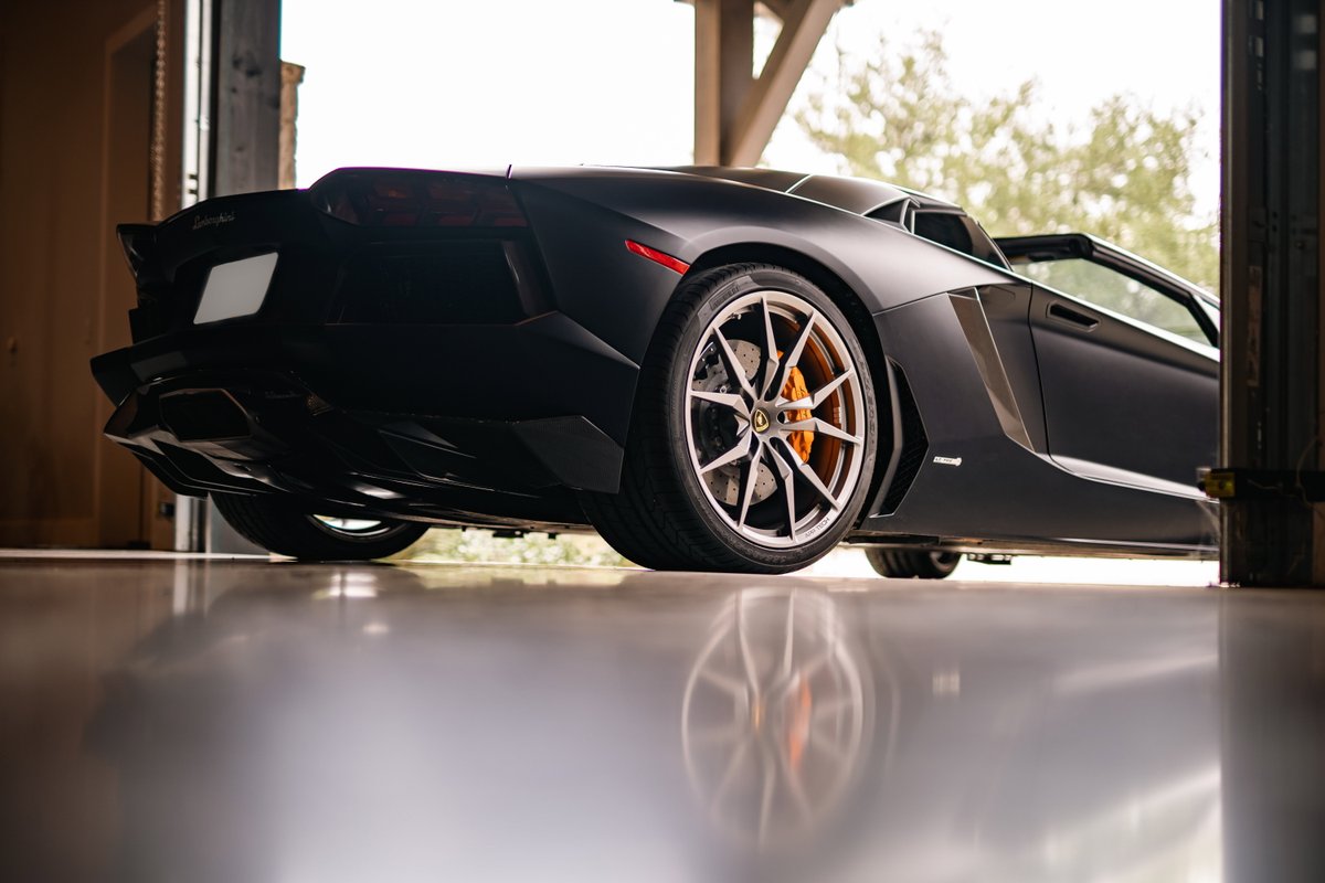 Matte black Lamborghini Aventador LP700-4 convertible with orange brake calipers and multi-spoke rims.