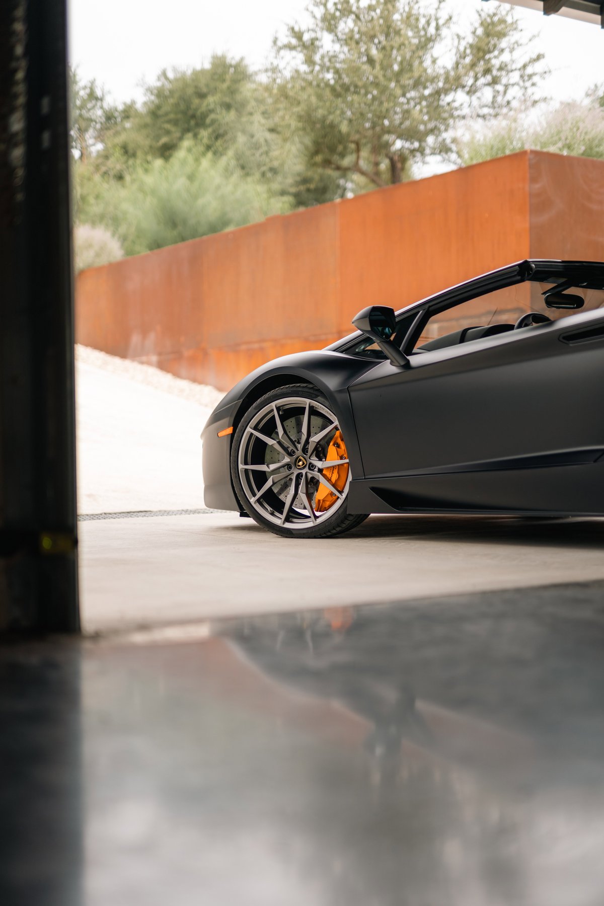 Matte black Lamborghini Aventador LP700-4 convertible with silver rims and orange brake calipers.