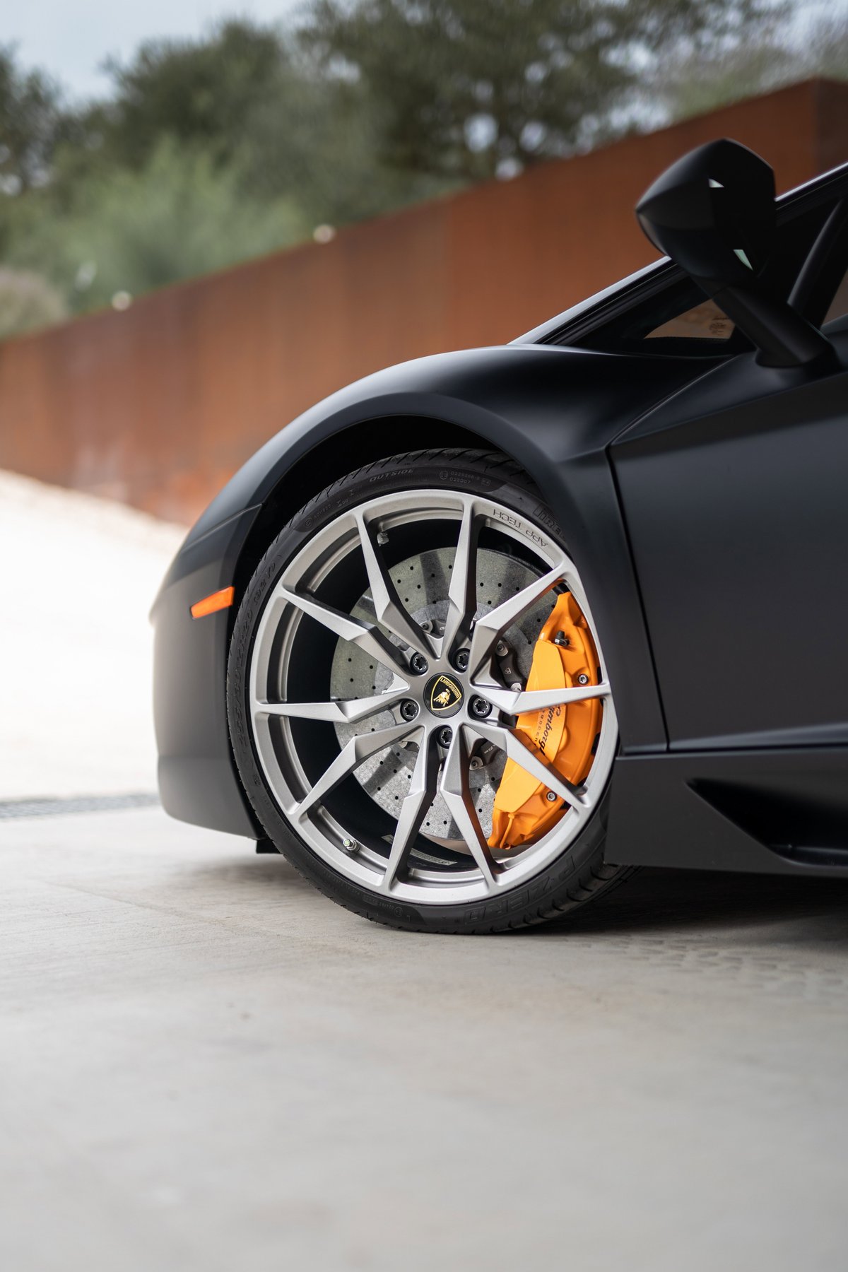 Matte black Lamborghini Aventador LP700-4 front wheel with orange brake calipers and silver rims.