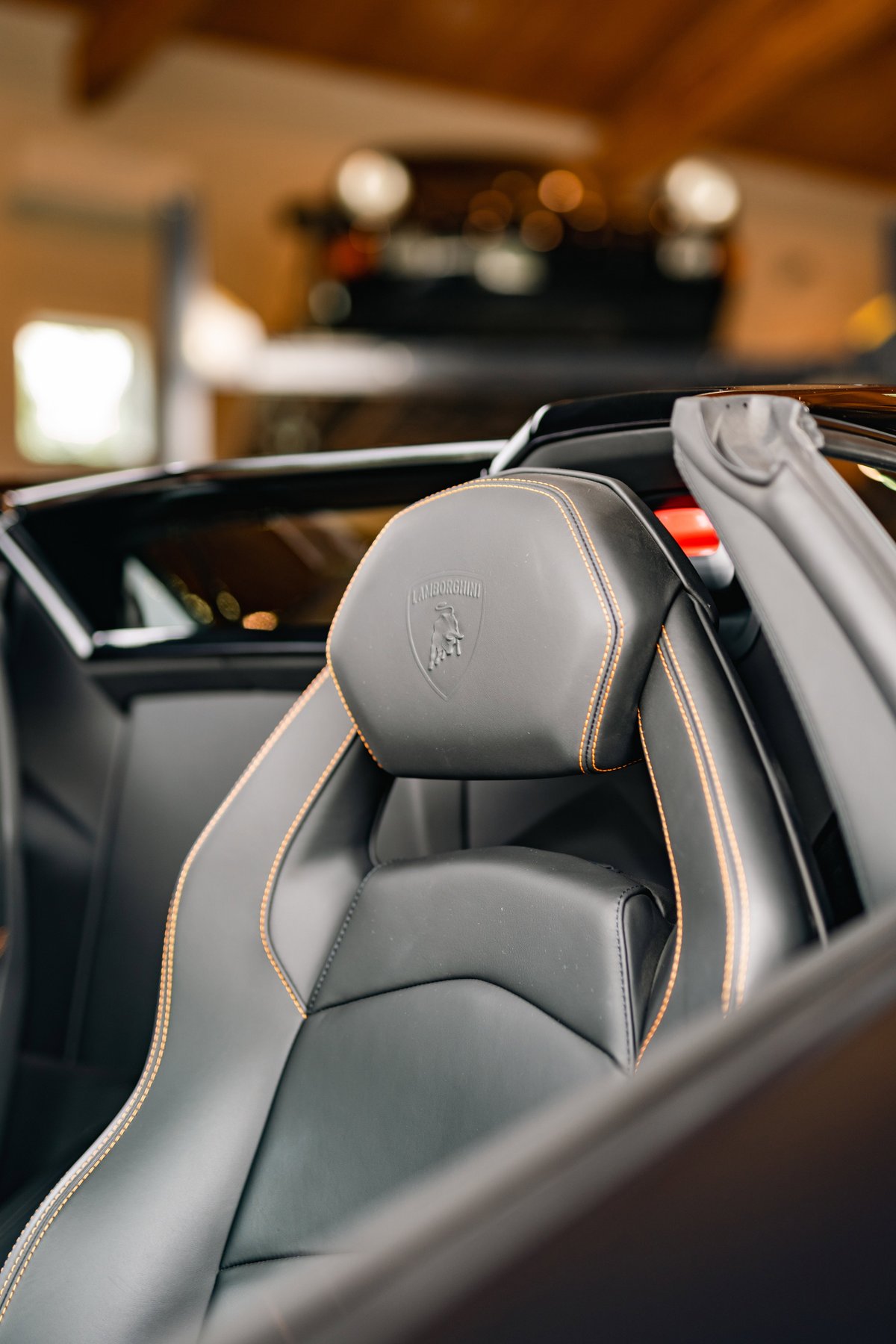 Black Lamborghini Aventador LP700-4 interior, featuring embossed shield and orange stitching on leather seats.
