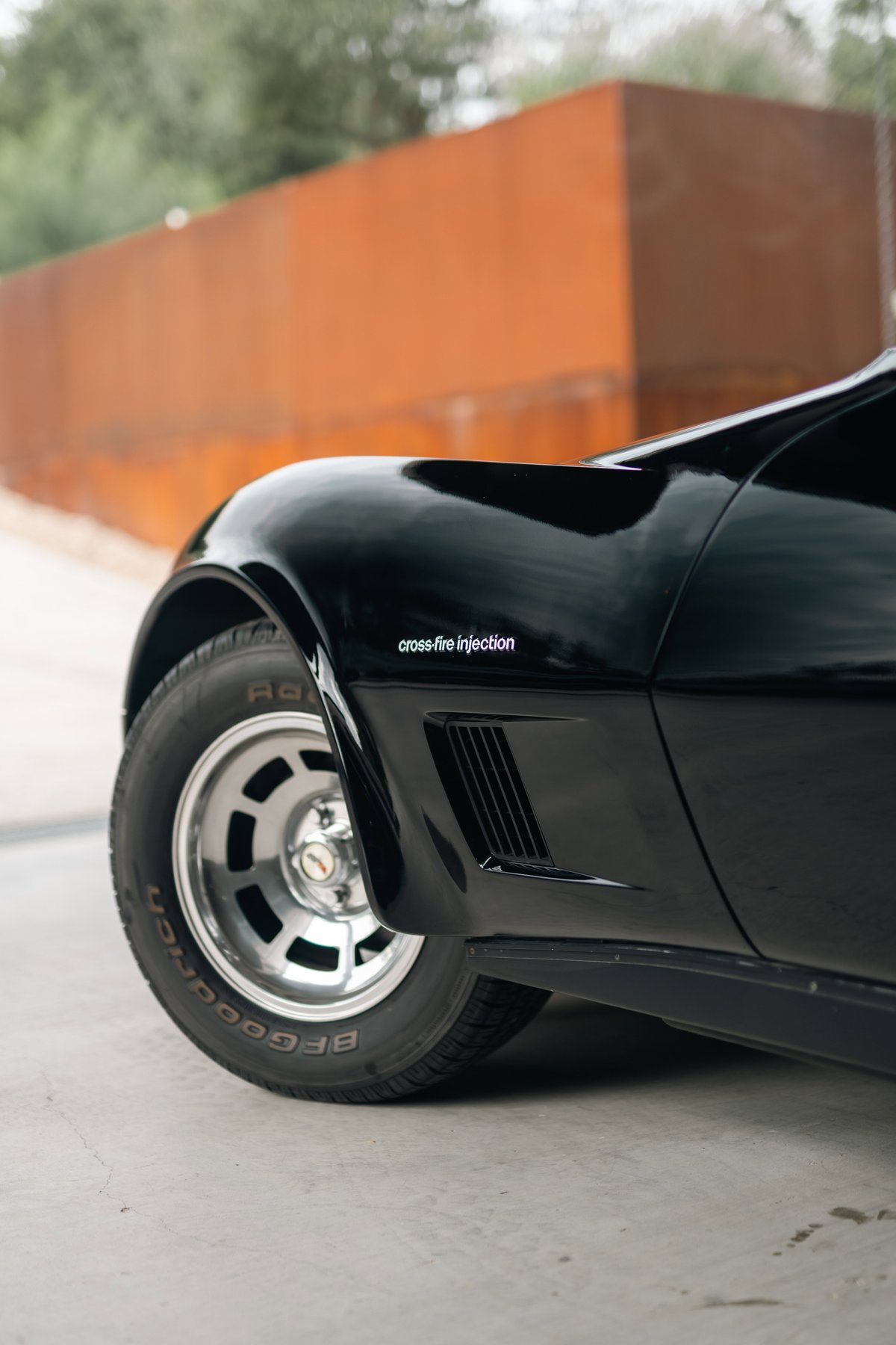 Close-up of a black 1982 Corvette Stingray fender with "Cross-Fire Injection" badging and a turbine-style rim.