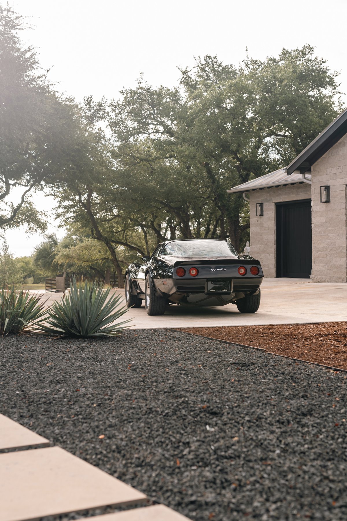 Rear view of a black 1982 Chevrolet Corvette Stingray with chrome rims, parked on a driveway.
