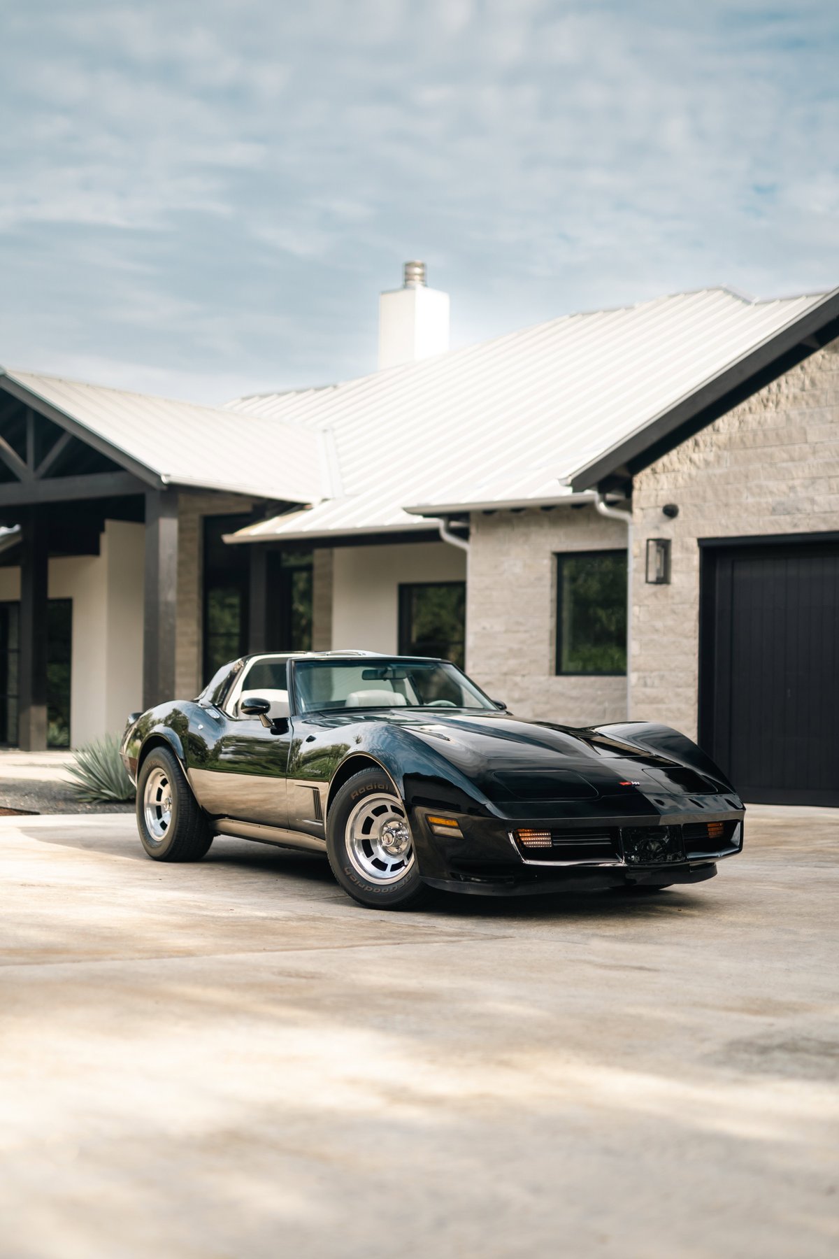 Black 1982 Chevrolet Corvette Stingray with polished aluminum rims parked in front of a modern home.