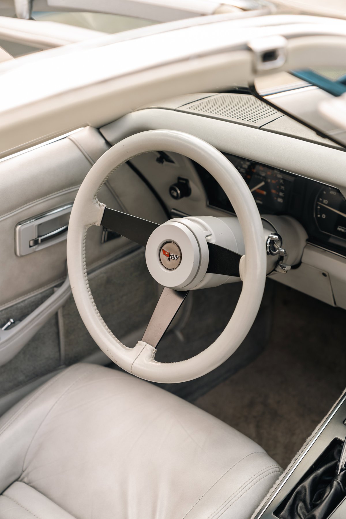 Close-up of a white 1982 Chevrolet Corvette Stingray interior, featuring a white leather steering wheel and seats.
