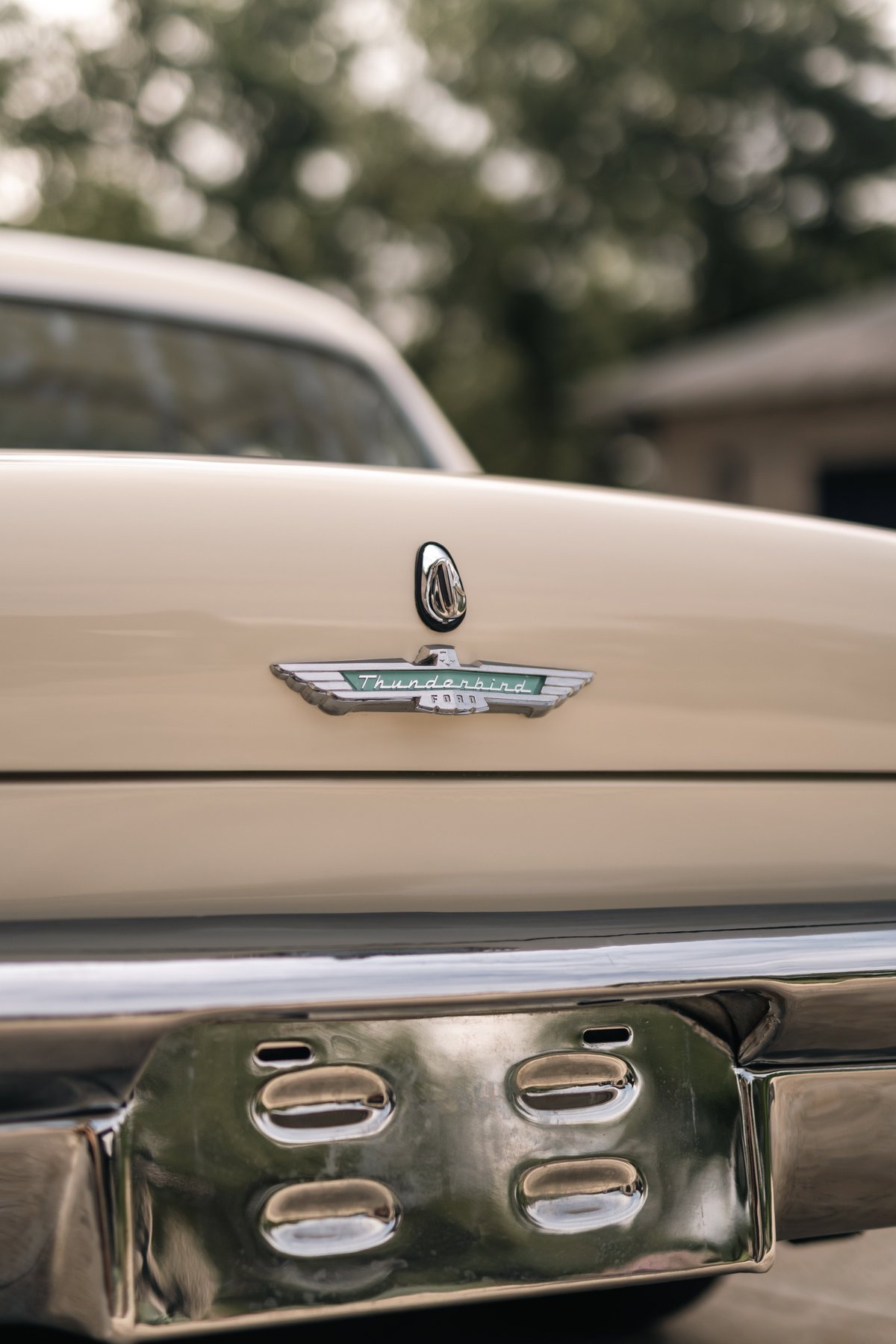 Close up of a colonial white 1957 Ford Thunderbird rear emblem and chrome bumper detail.