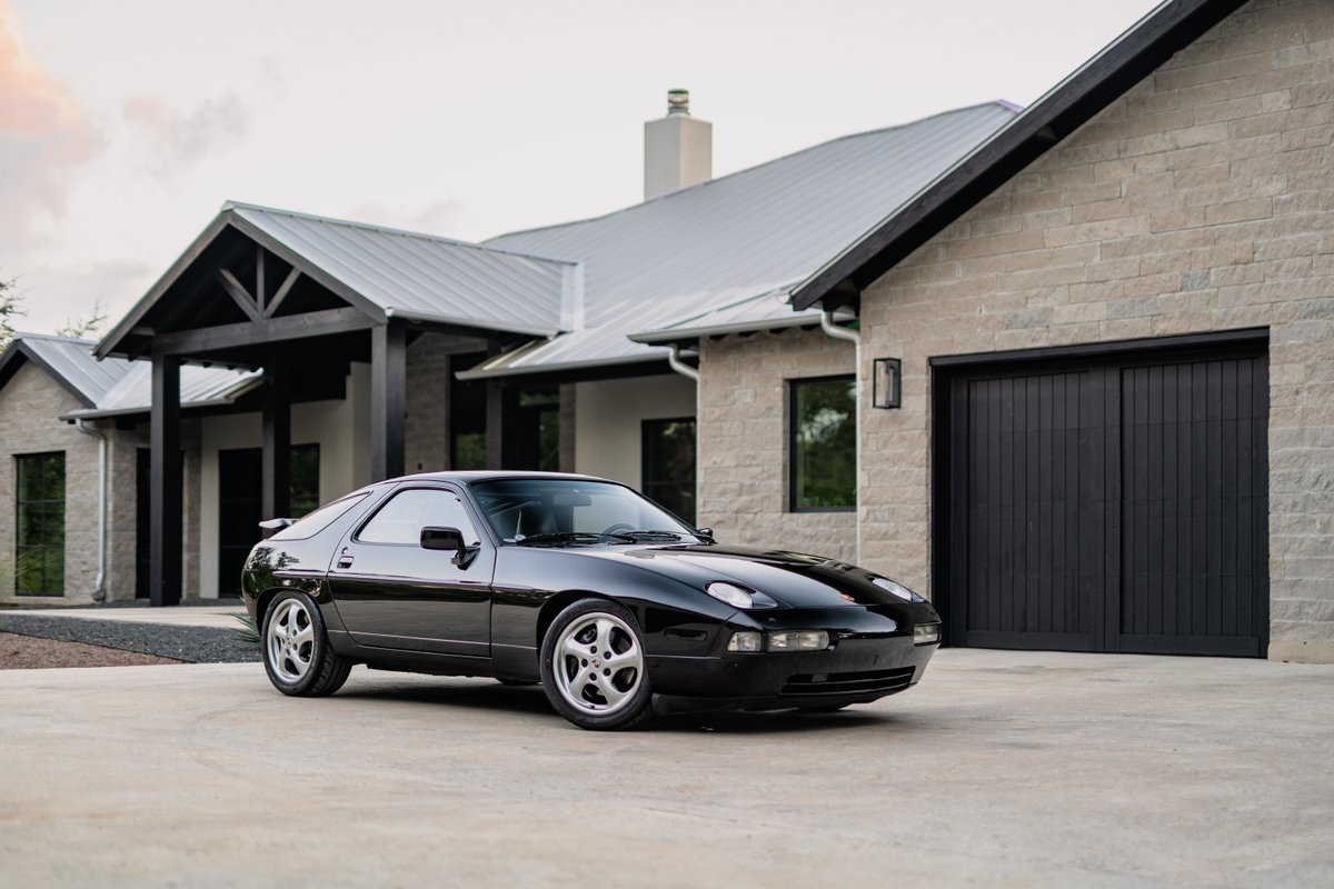 Black 1984 Porsche 928S with turbine-style rims parked in front of a modern home.