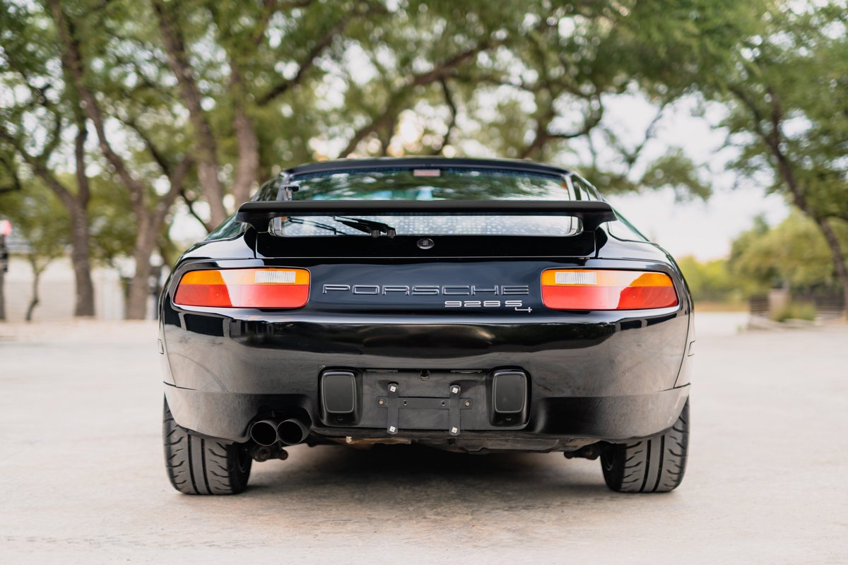 Rear view of a black 1984 Porsche 928 S4, featuring quad exhaust tips and a rear spoiler.