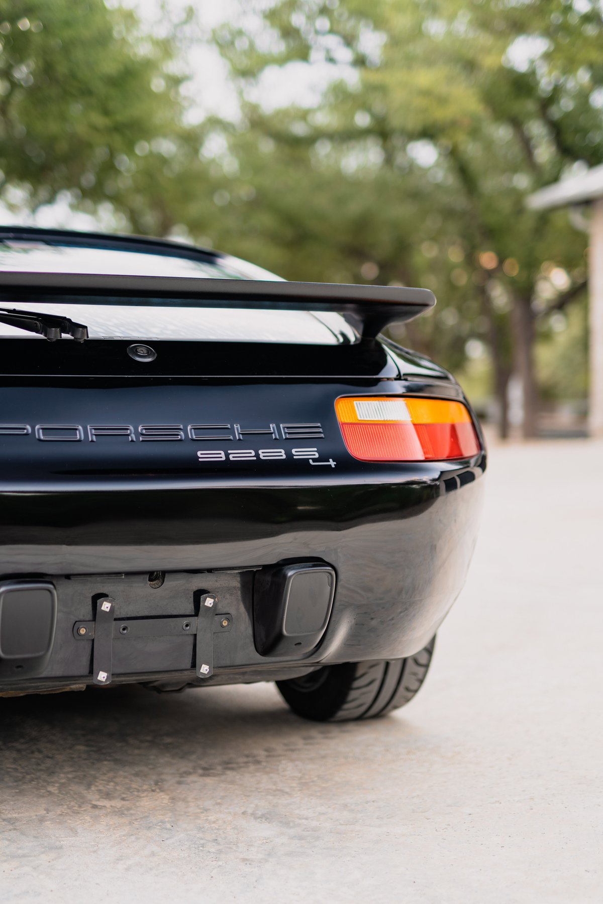 Black 1984 Porsche 928 S4 rear, showing taillight, spoiler, and exhaust.