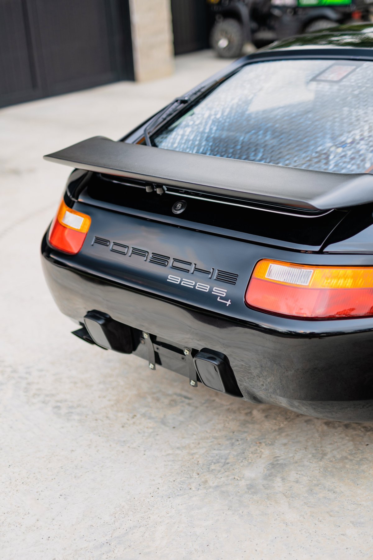Rear view of a black Porsche 928 S4 with a spoiler and dual exhaust tips.