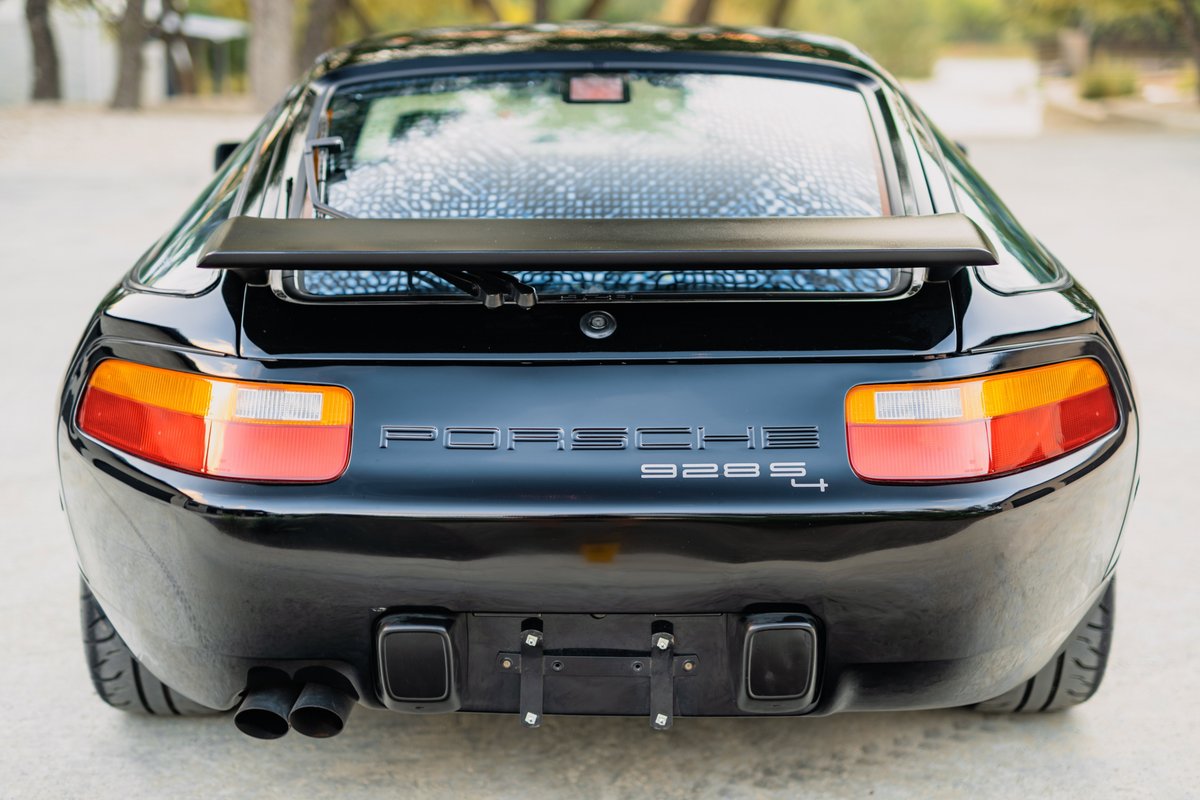 Rear view of a black 1984 Porsche 928 S4 with a spoiler, quad exhaust pipes, and iconic badging.