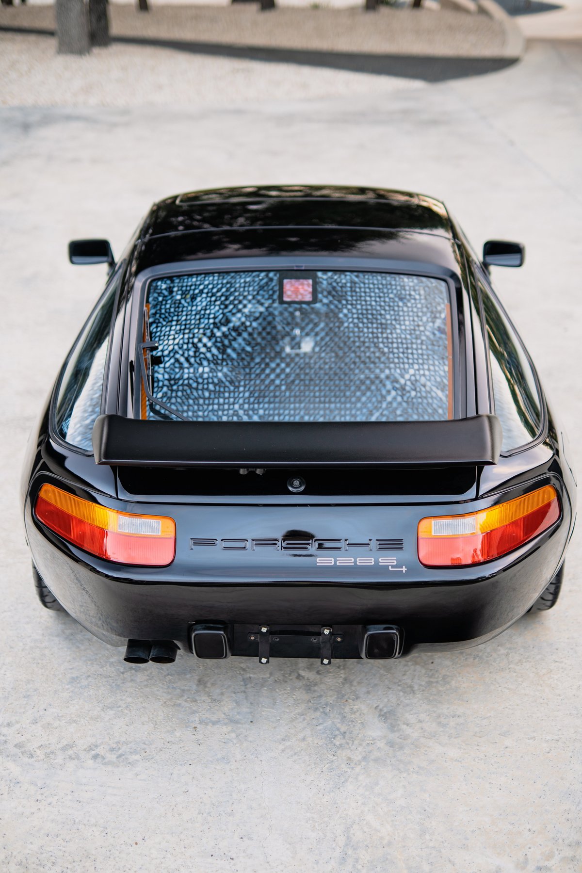 Rear view of a black 1984 Porsche 928 S4 with quad exhaust tips and a rear spoiler.