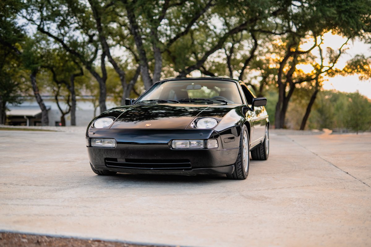 Front view of a black 1984 Porsche 928 S4 with its iconic pop-up headlights and clean trim.