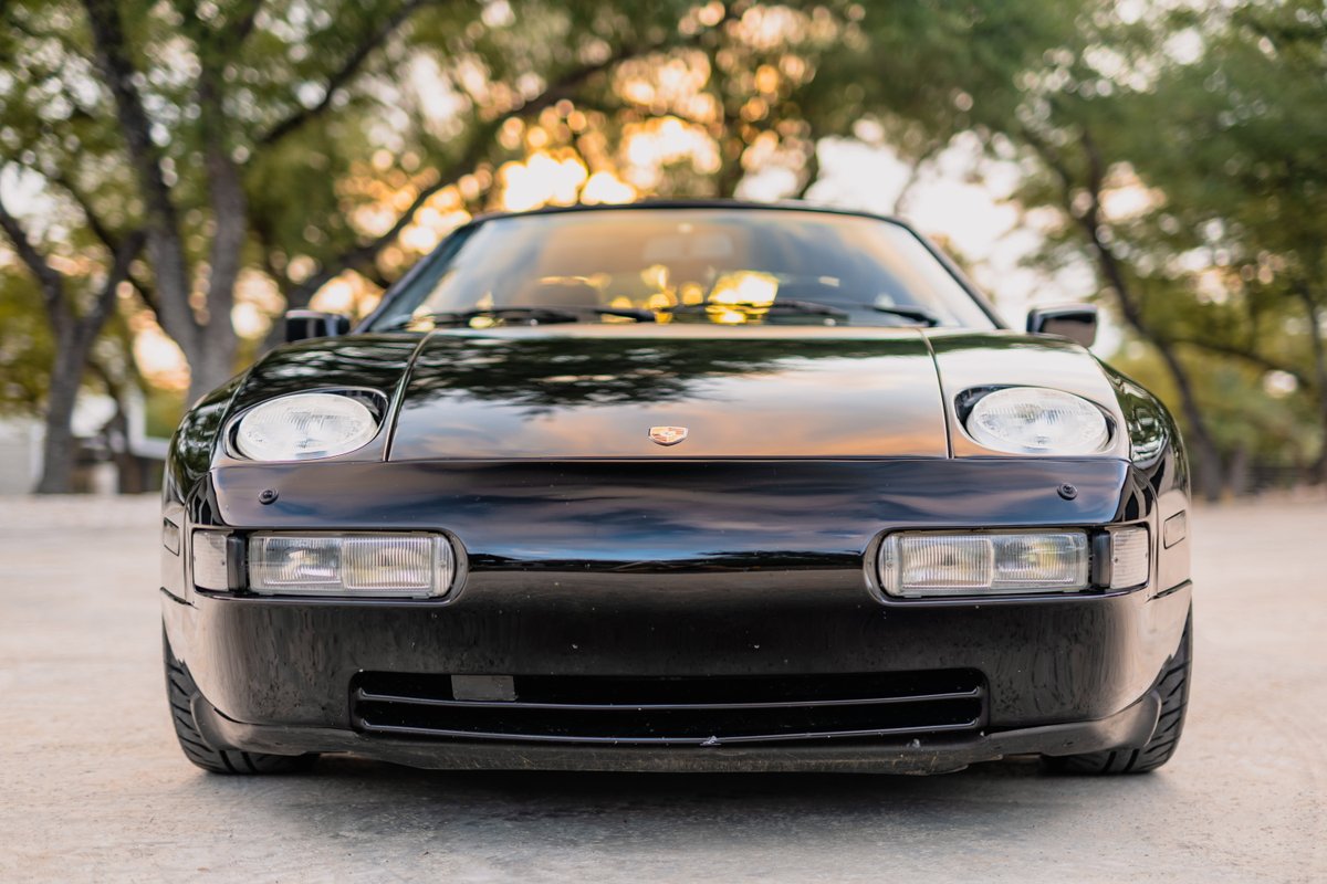 Front view of a black 1984 Porsche 928 S4 with pop-up headlights and clean trim.