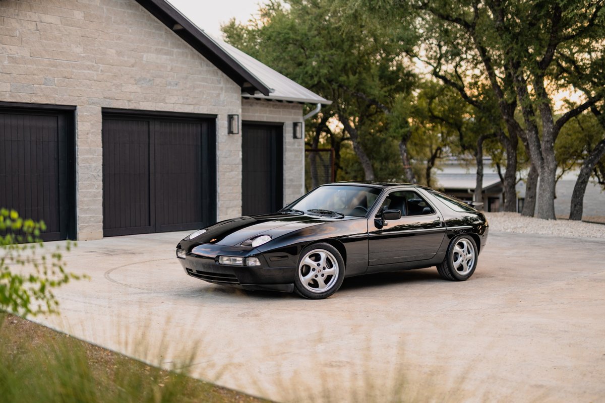 Black 1984 Porsche 928 S4 coupe on turbine-style alloy rims parked outside a modern home.