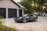 Black 1984 Porsche 928 S4 coupe on turbine-style alloy rims parked outside a modern home.