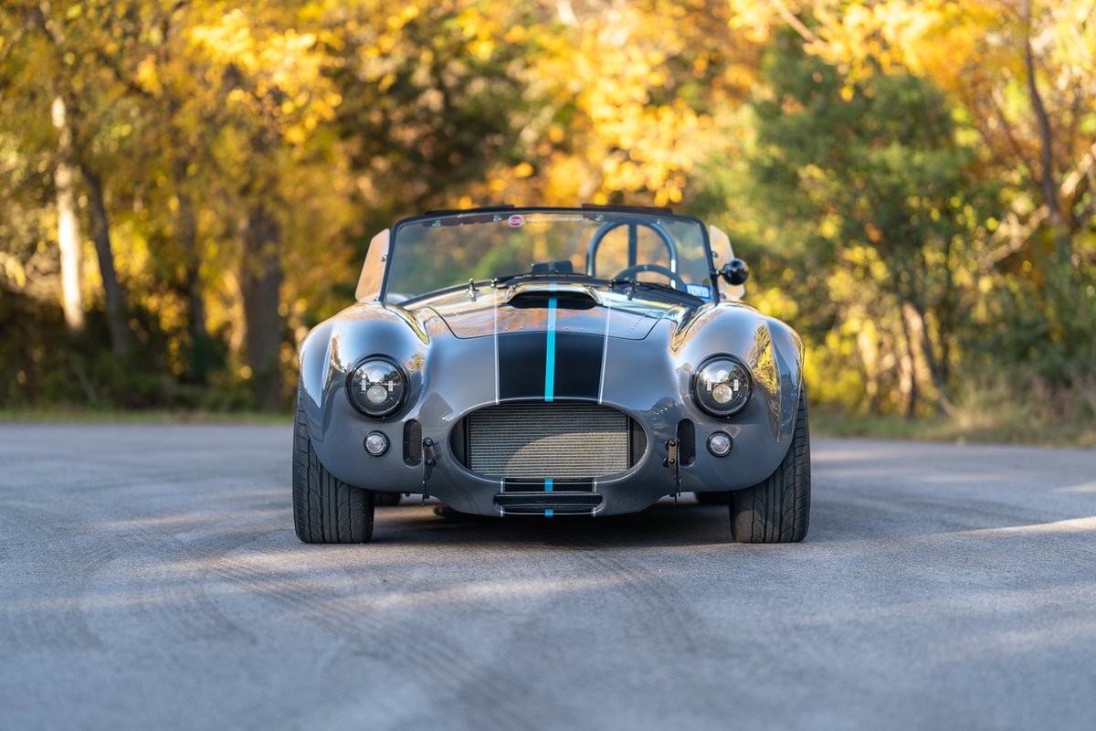 Front view of a gray 1965 Backdraft Cobra with black and blue racing stripes.