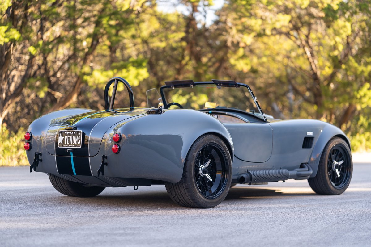 Gray 1965 Backdraft Cobra with dual black racing stripes and blue accent. Black rims and roll bar.