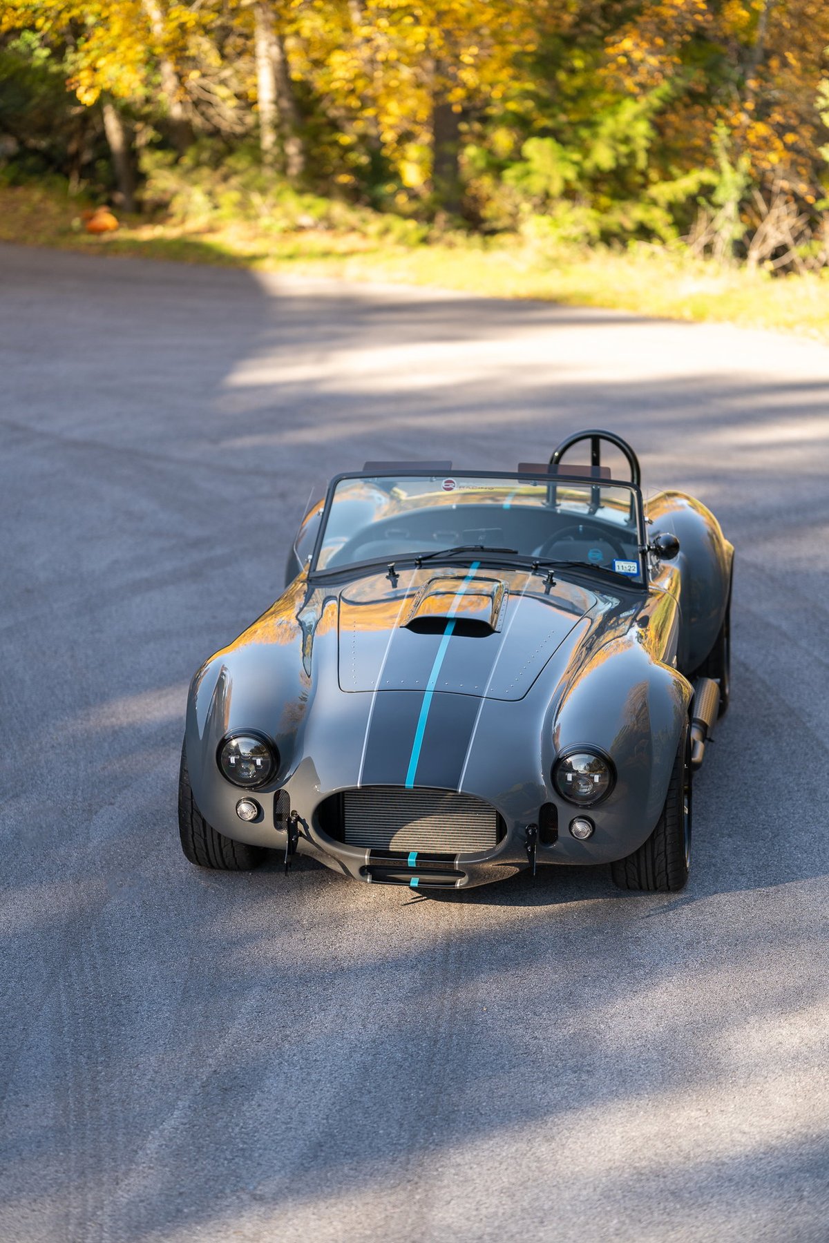 A gray 1965 Backdraft Cobra with blue racing stripes and chrome rims.
