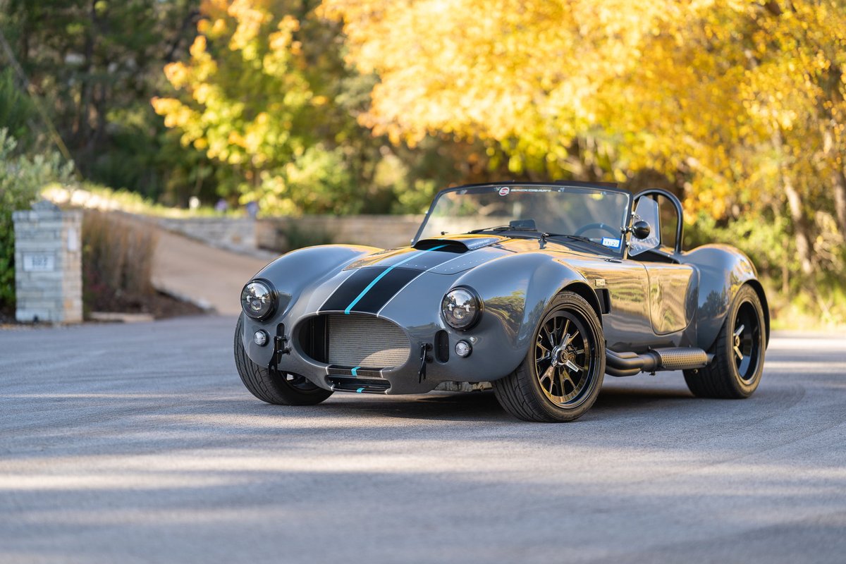 Gray 1965 Backdraft Cobra with dual blue racing stripes and black rims.