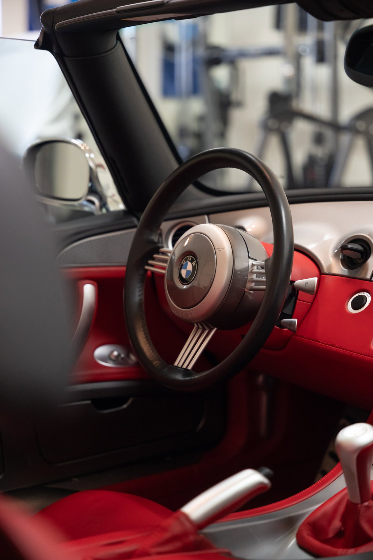 Interior of a titanium silver 2002 BMW Z8 convertible, featuring red leather trim and a classic steering wheel.