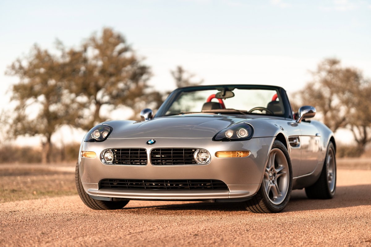 Front 3/4 view of a silver 2002 BMW Z8 convertible with chrome rims on a dirt road.