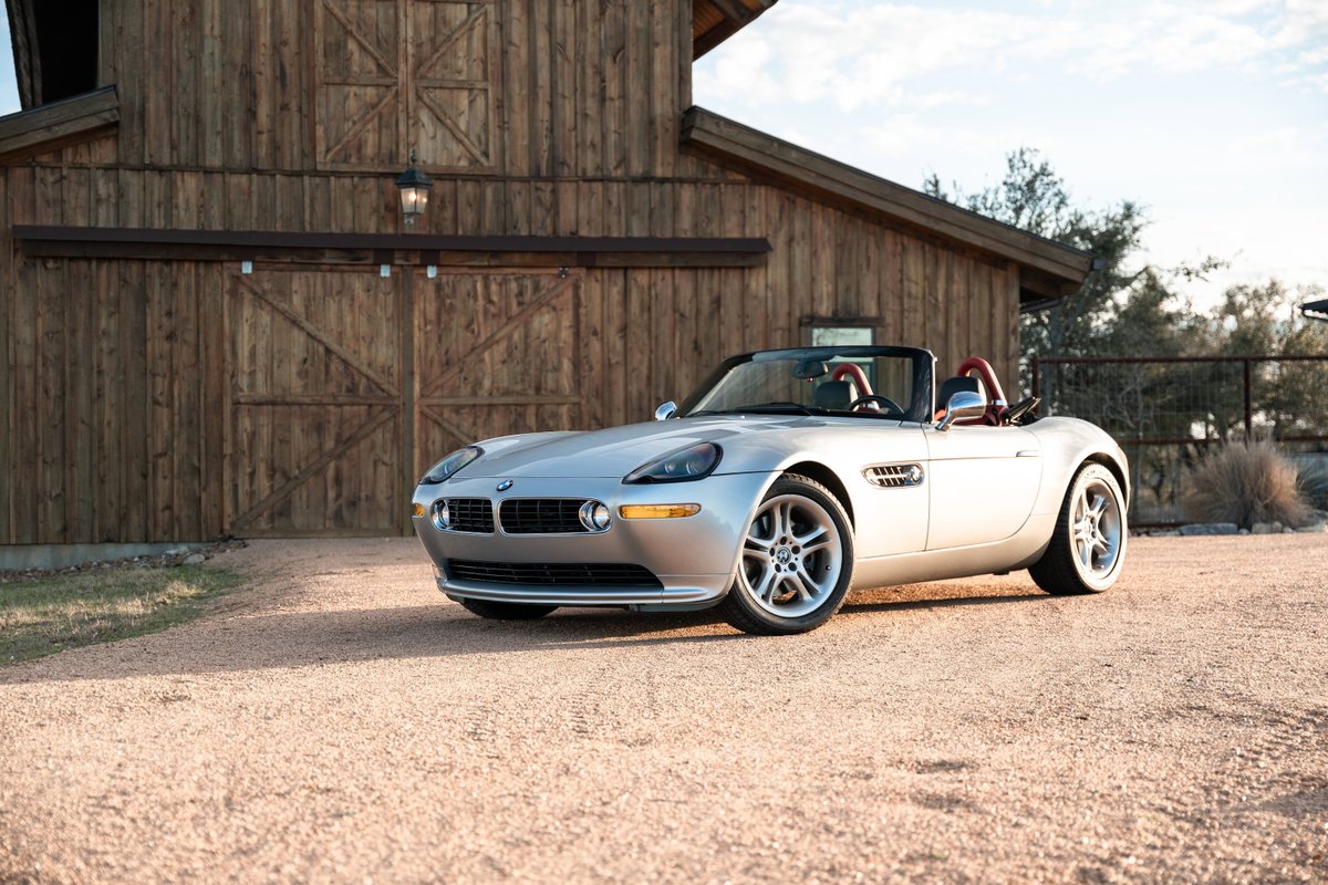Silver 2002 BMW Z8 roadster with red interior, parked outside a rustic barn.