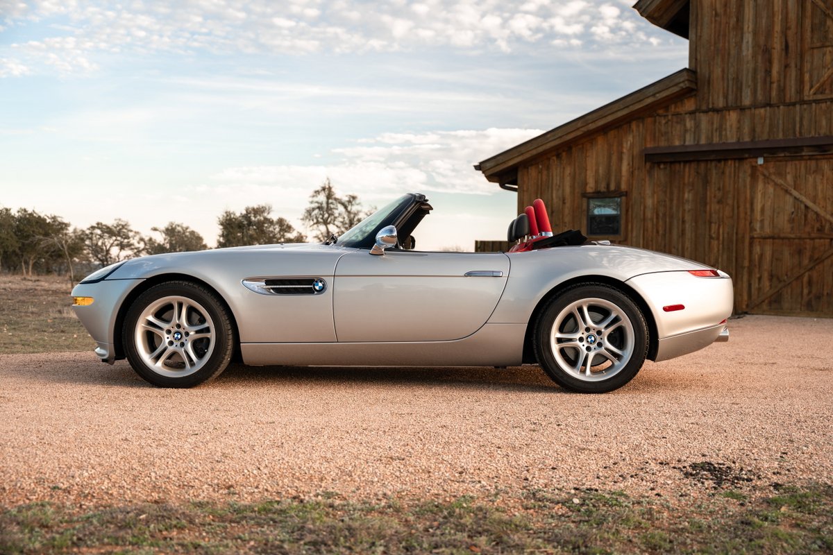 Silver 2002 BMW Z8 convertible with red interior, parked outside a wooden barn.
