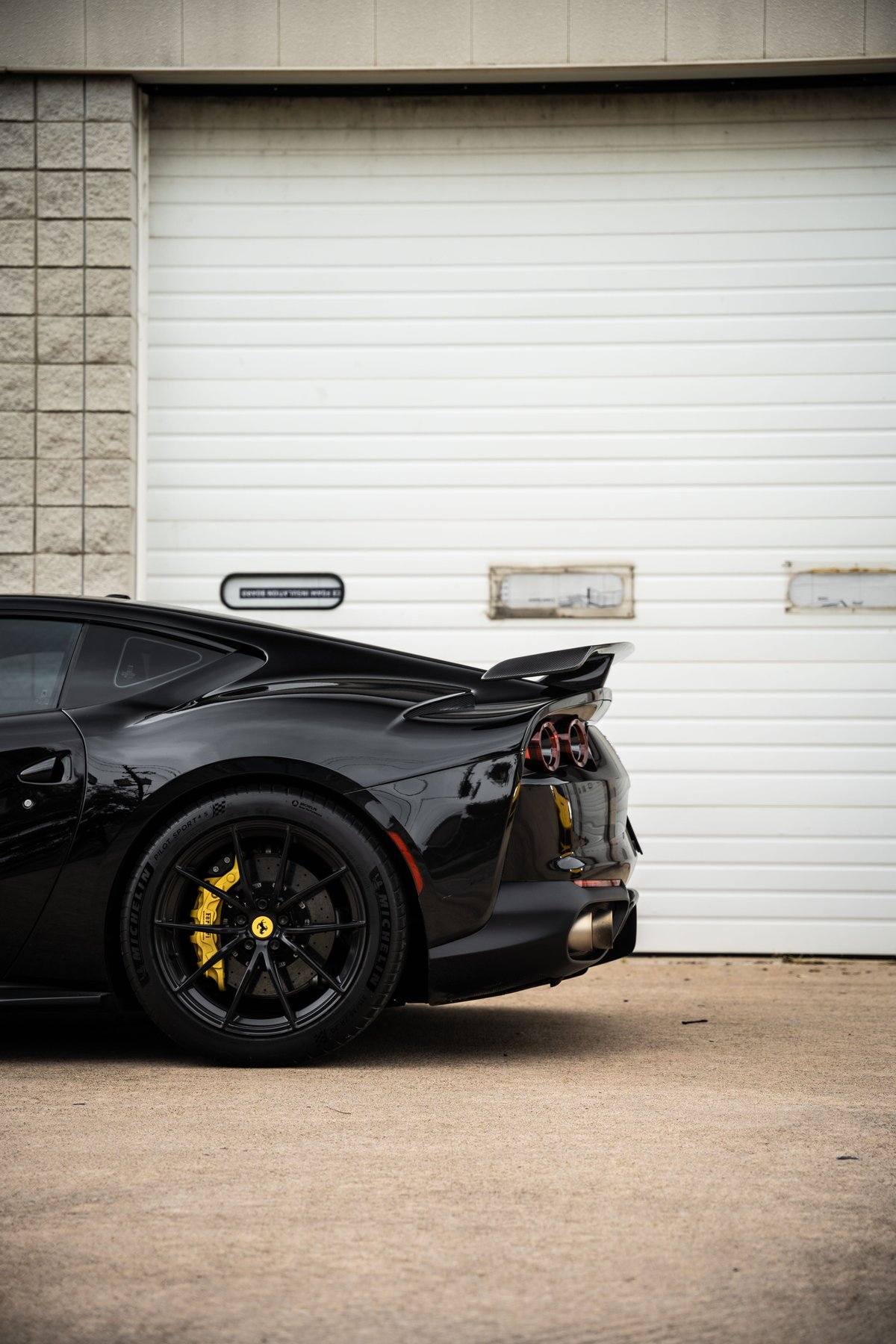 Black Ferrari 812 Superfast rear quarter panel view, black rims, yellow brake calipers, active aero wing.