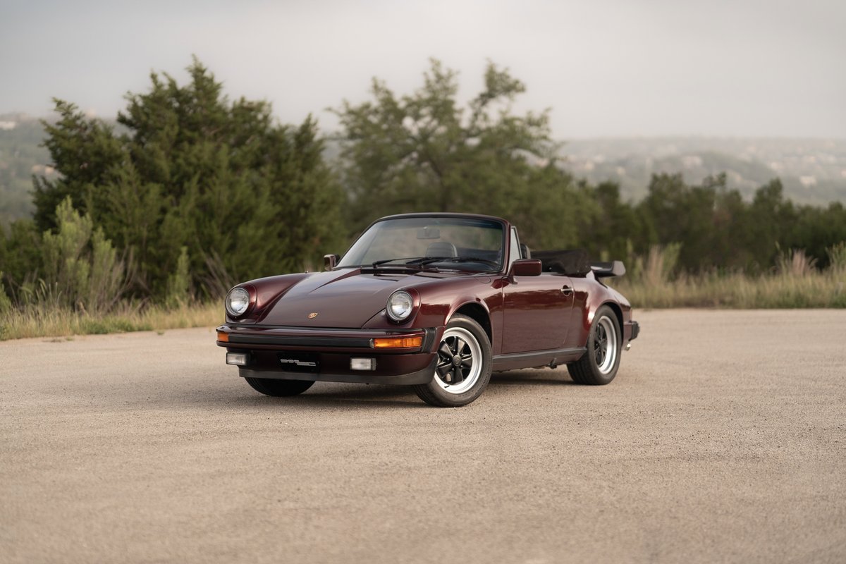 A ruby red metallic 1983 Porsche 911SC Cabriolet with Fuchs rims and black trim.