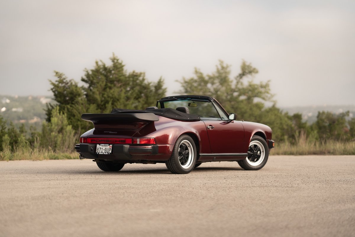 Rear view of a ruby red metallic 1983 Porsche 911 SC Cabriolet with whale tail spoiler and black trim.