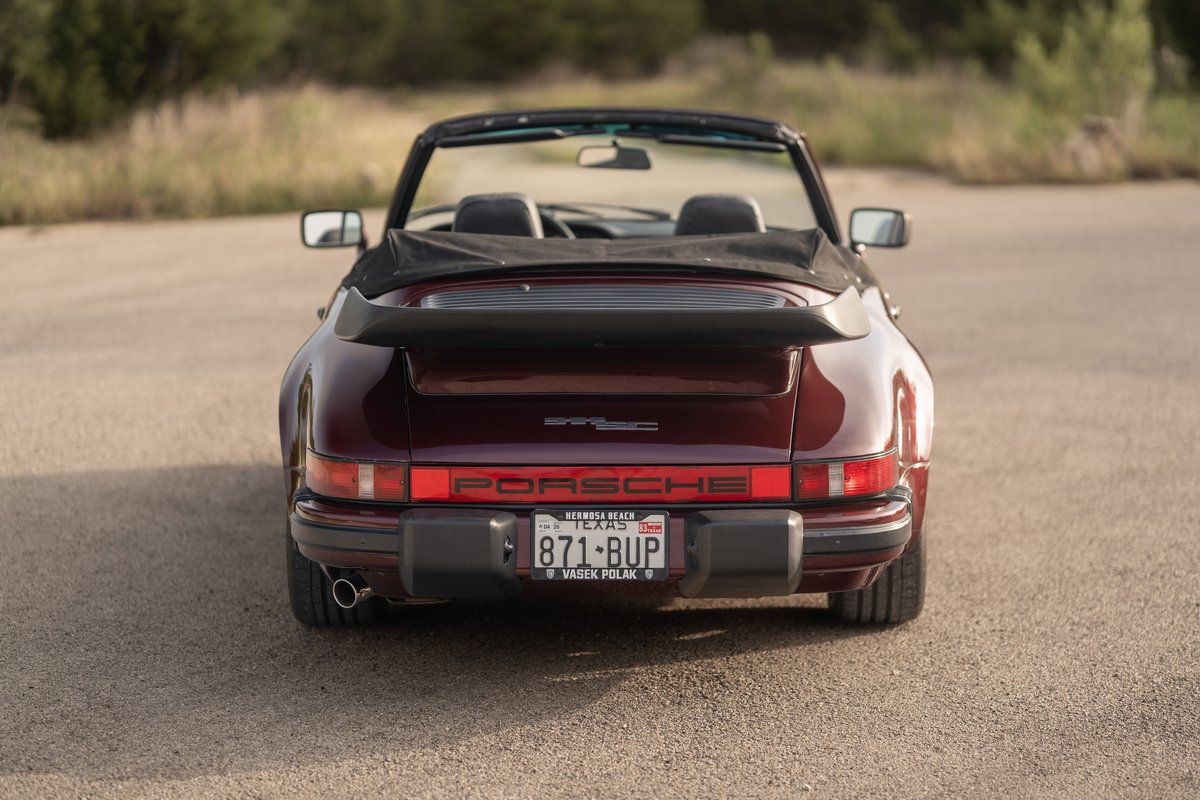 Rear view of a ruby red metallic 1983 Porsche 911 SC convertible with black trim and a whale tail spoiler.