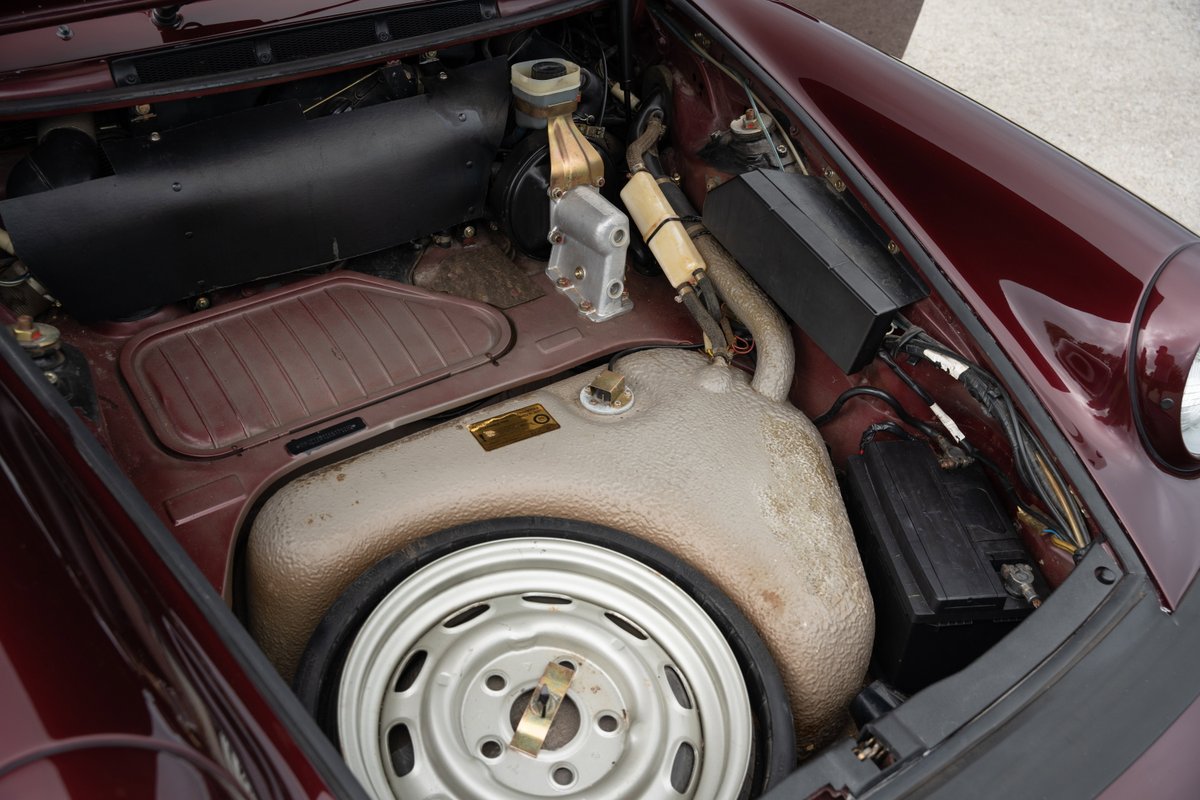 1983 Porsche 911 SC Cabriolet engine bay, ruby red metallic, spare tire and battery visible.