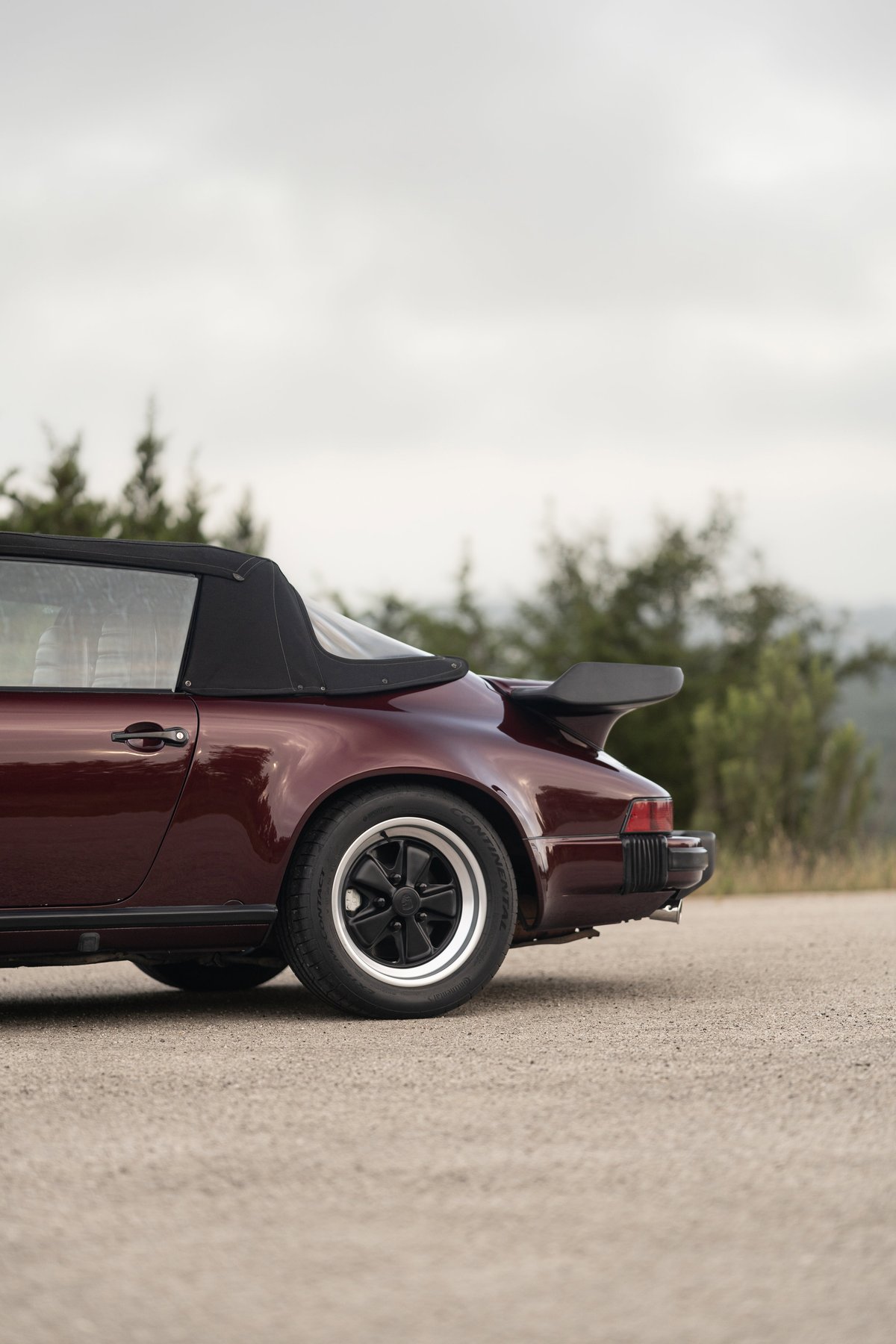 Ruby red 1983 Porsche 911 SC Cabriolet with a black soft top and iconic whale tail spoiler.