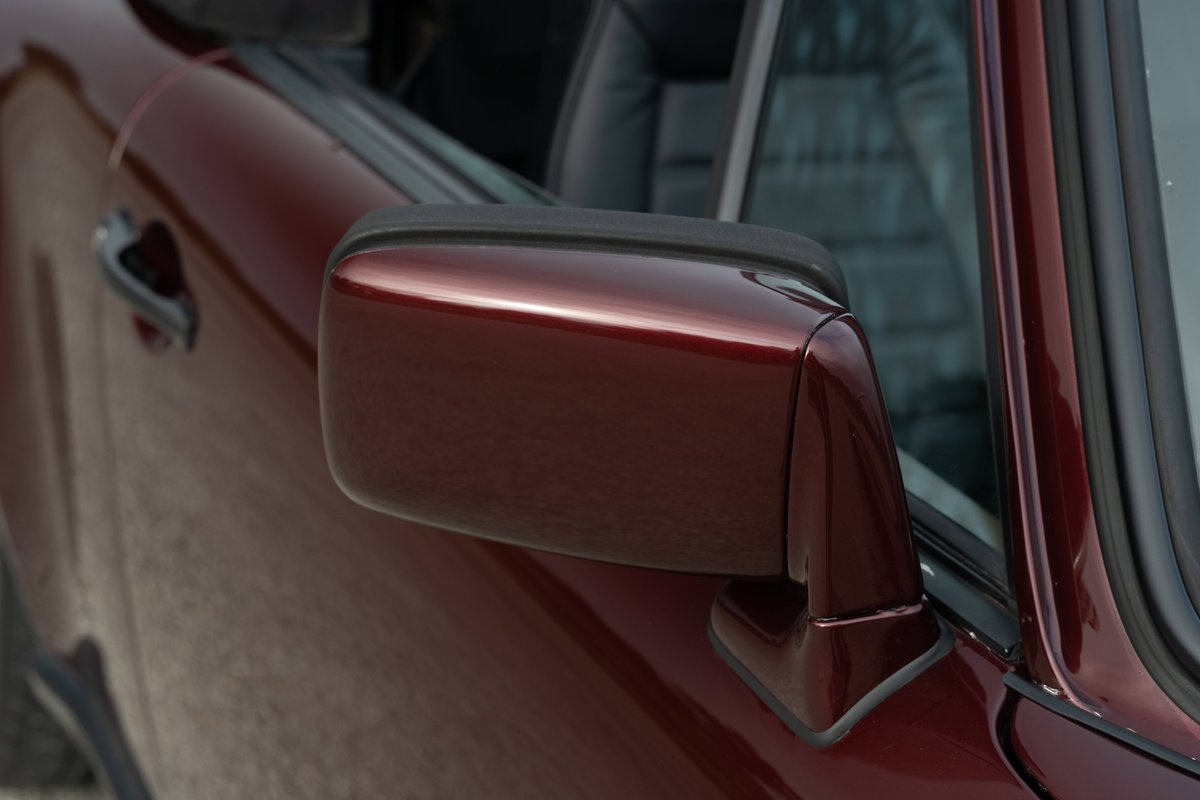 Close-up of a ruby red metallic 1983 Porsche 911SC Cabriolet, featuring the side mirror and door panel.