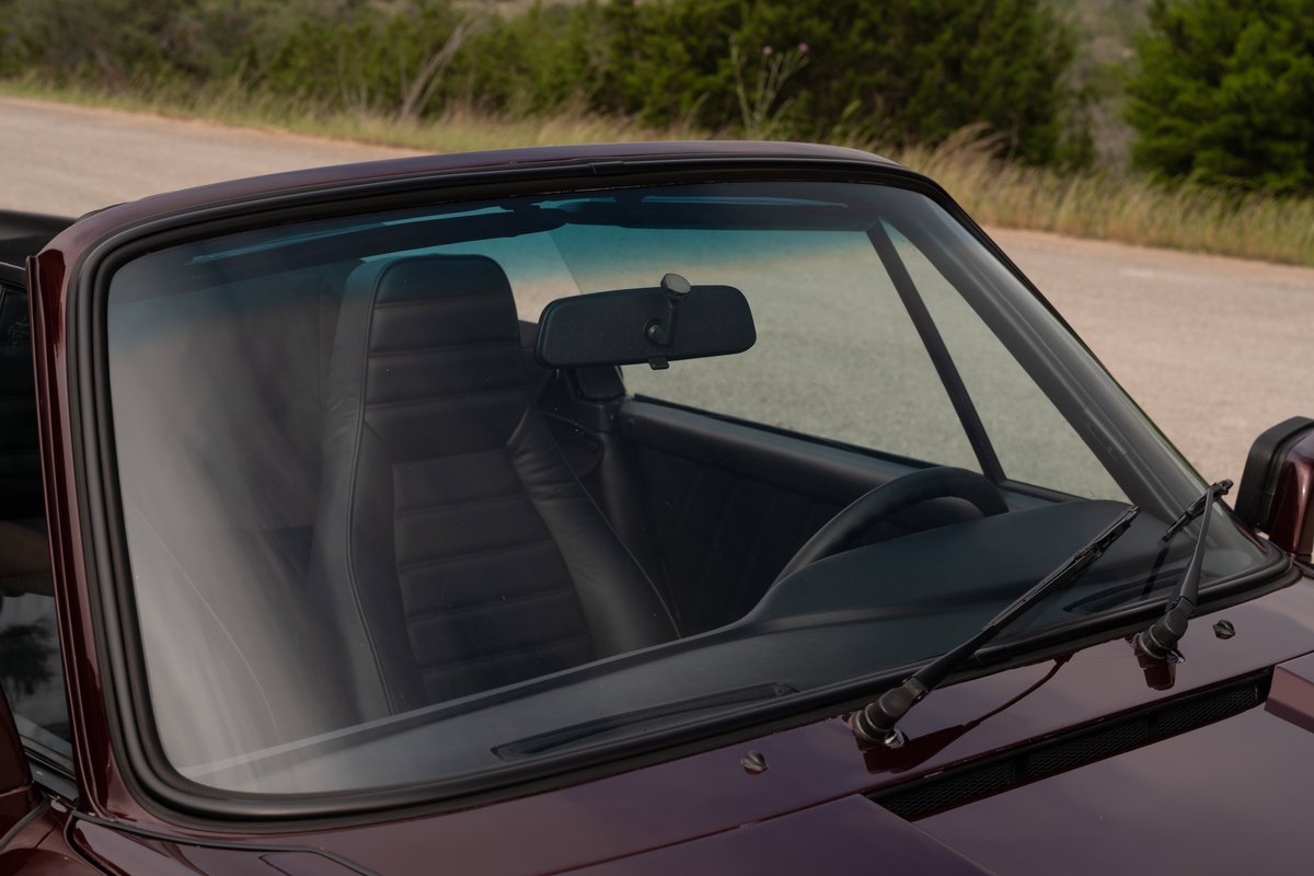Ruby red metallic 1983 Porsche 911 SC Cabriolet interior, black leather seats, dashboard, steering wheel.