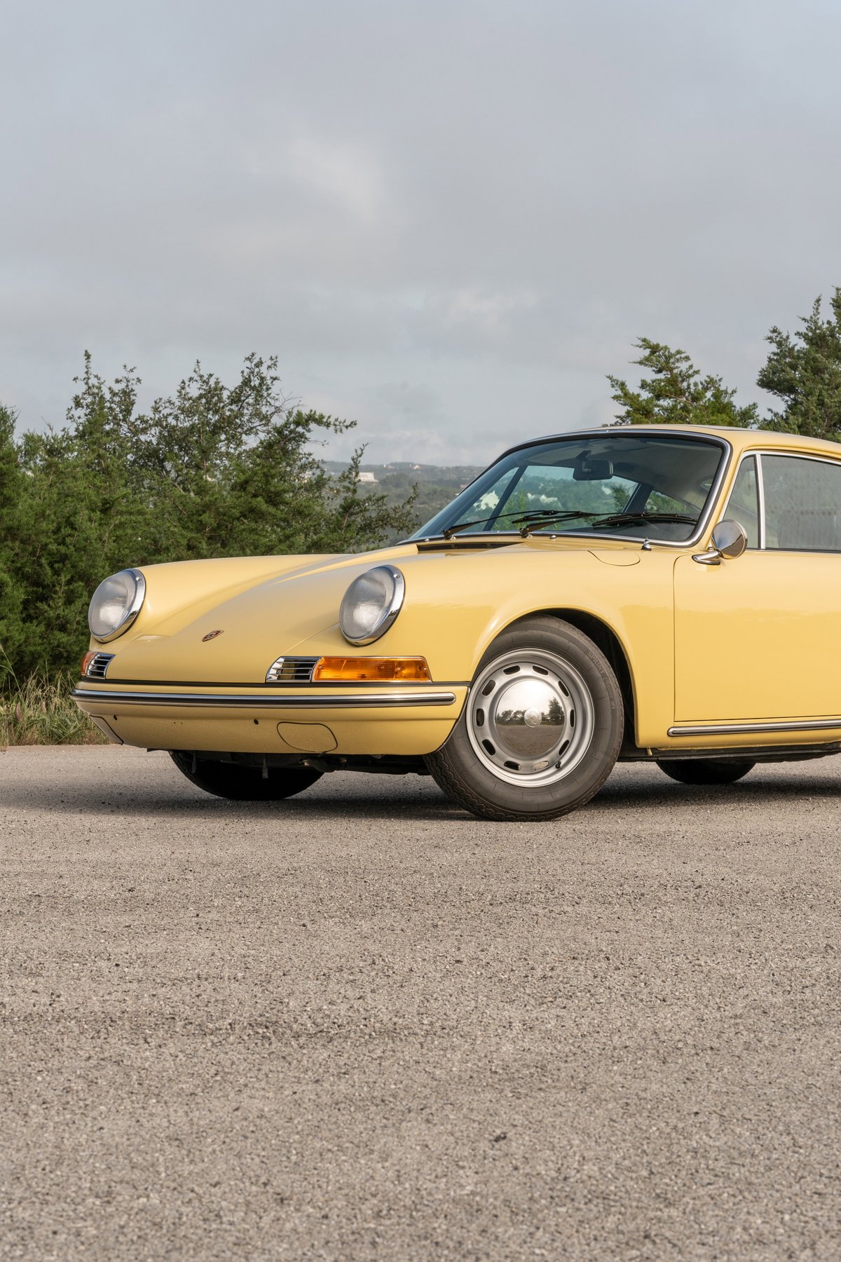 Close-up of a champagne yellow 1969 Porsche 912 coupe front fender, showing chrome trim and hubcaps.