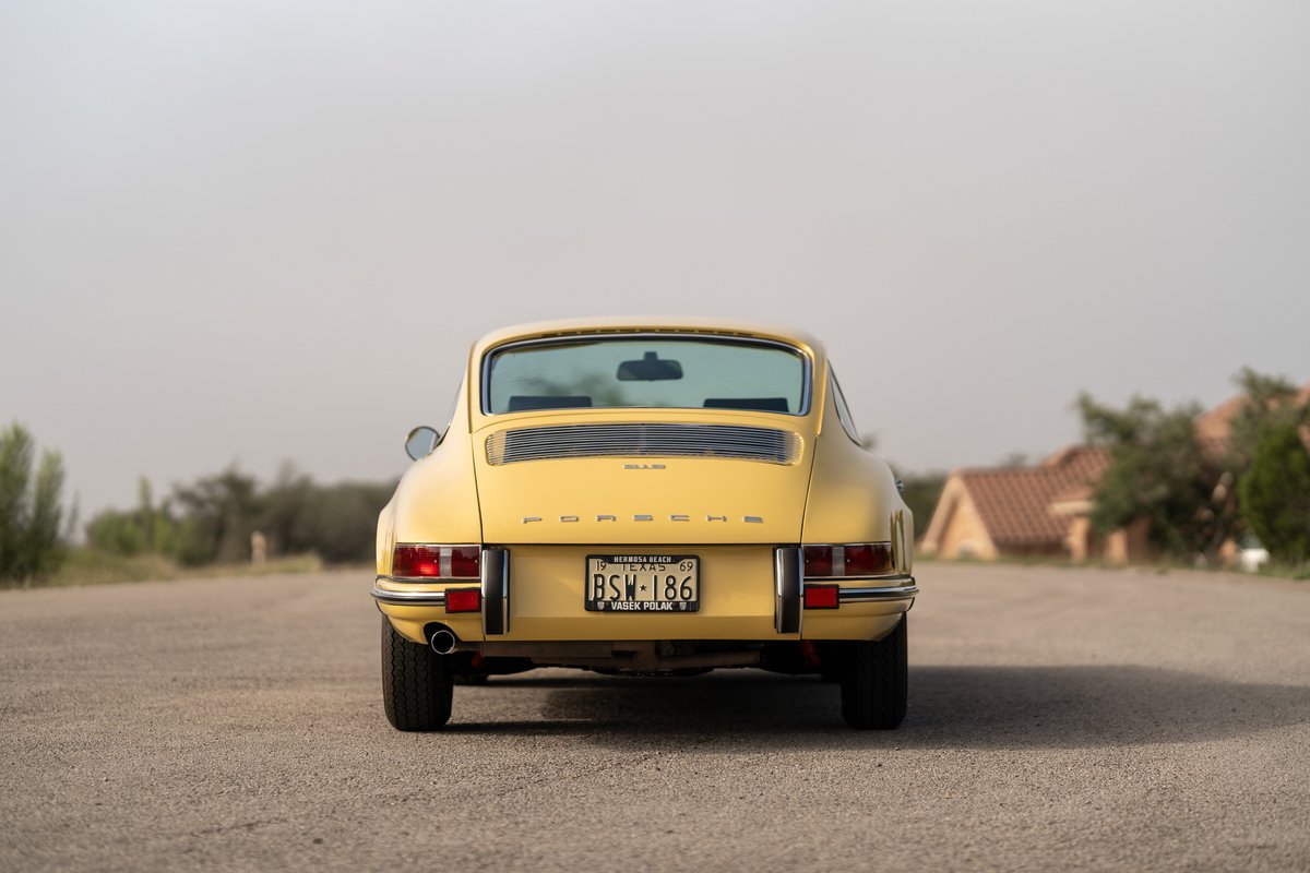 Rear view of a champagne yellow 1969 Porsche 912 coupe with chrome trim and classic rims.