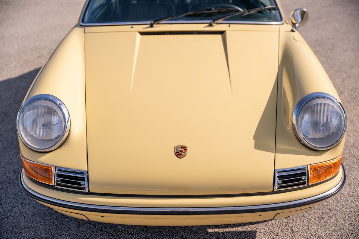 Close-up of a champagne yellow 1969 Porsche 912 coupe's front end. Chrome trim and round headlights.