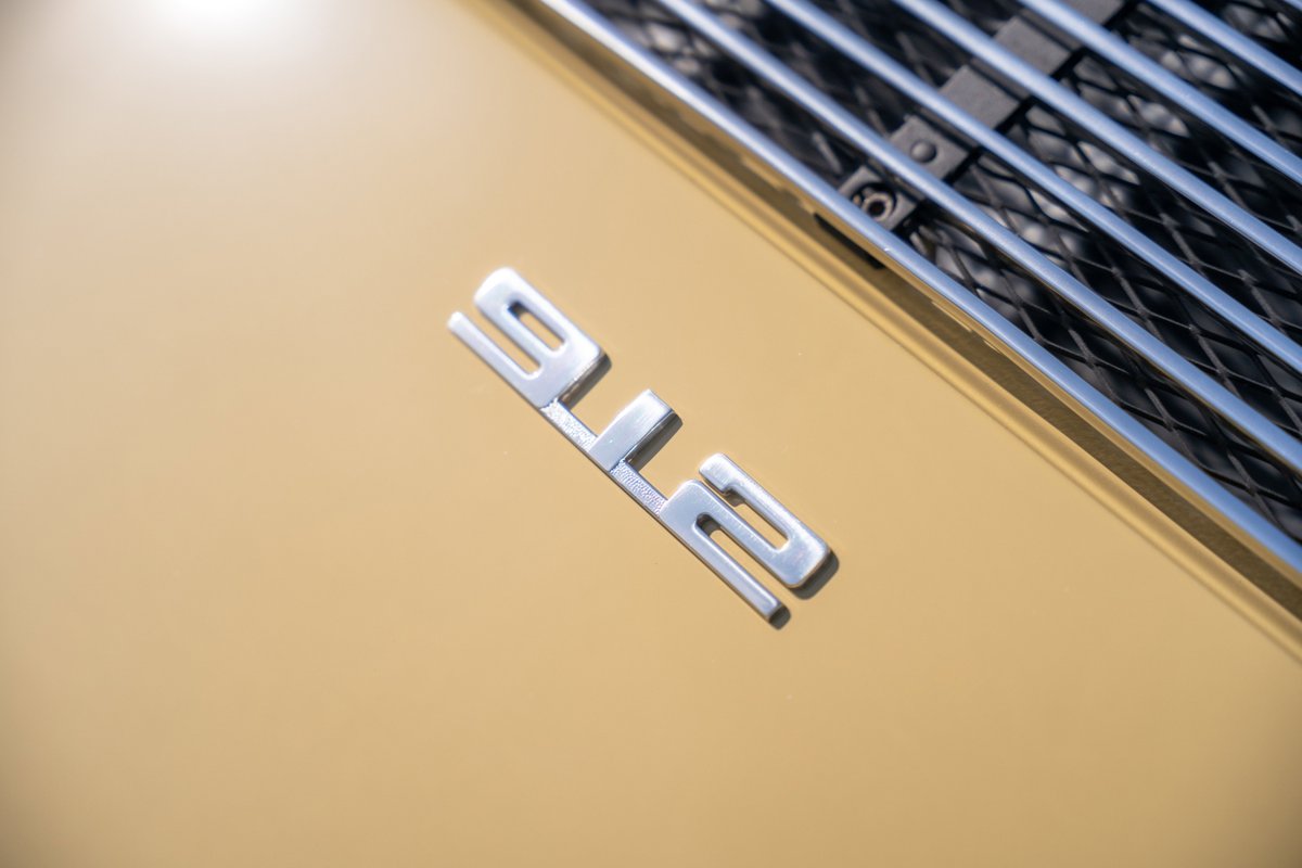 Close-up of a silver "912" badge on the champagne yellow body of a 1969 Porsche 912 coupe.