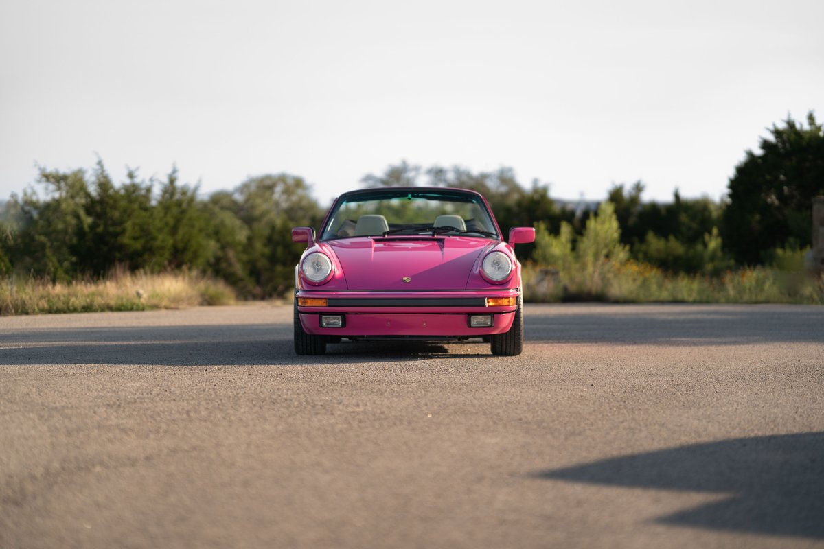 Front view of a pink Porsche 911 convertible with a black top, tan interior, and chrome rims.